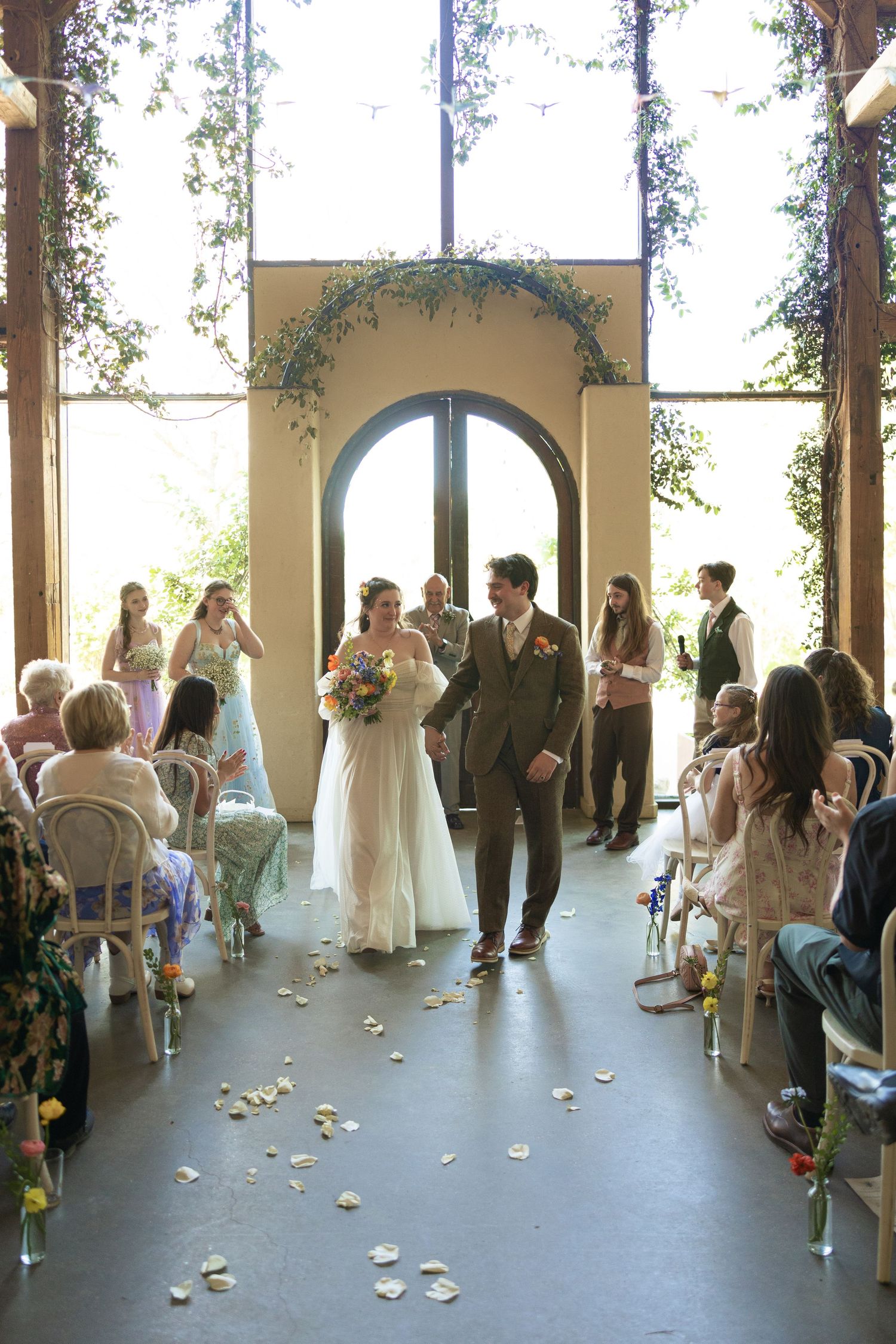 Wedding ceremony in progress at a covered outdoor venue with flower petals lining the aisle.