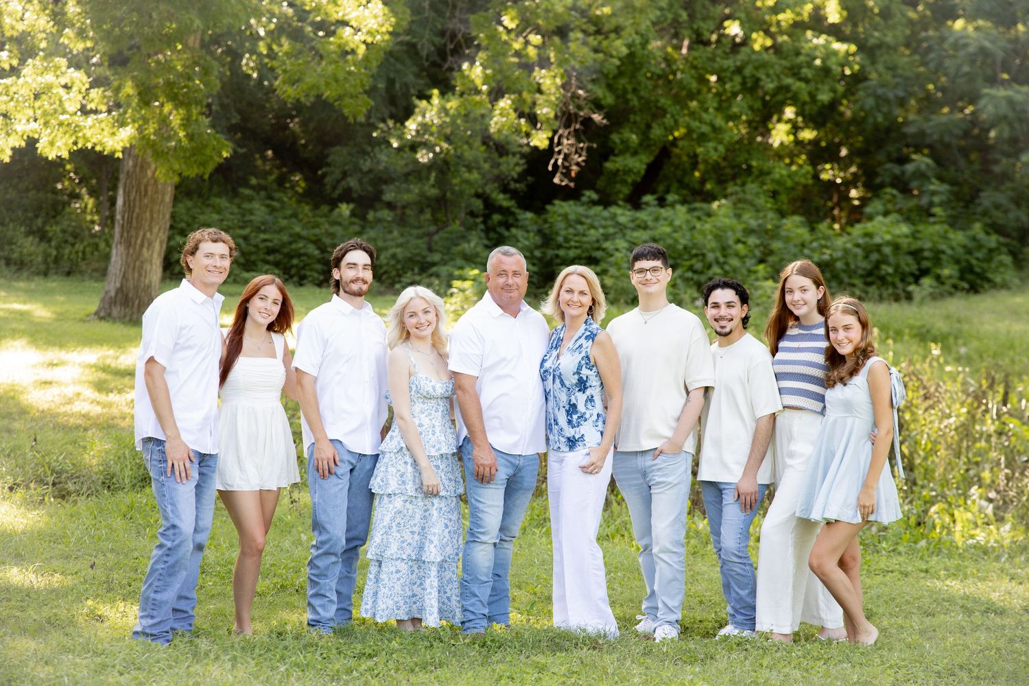 Family group portrait with coordinated white and blue outfits against natural greenery.