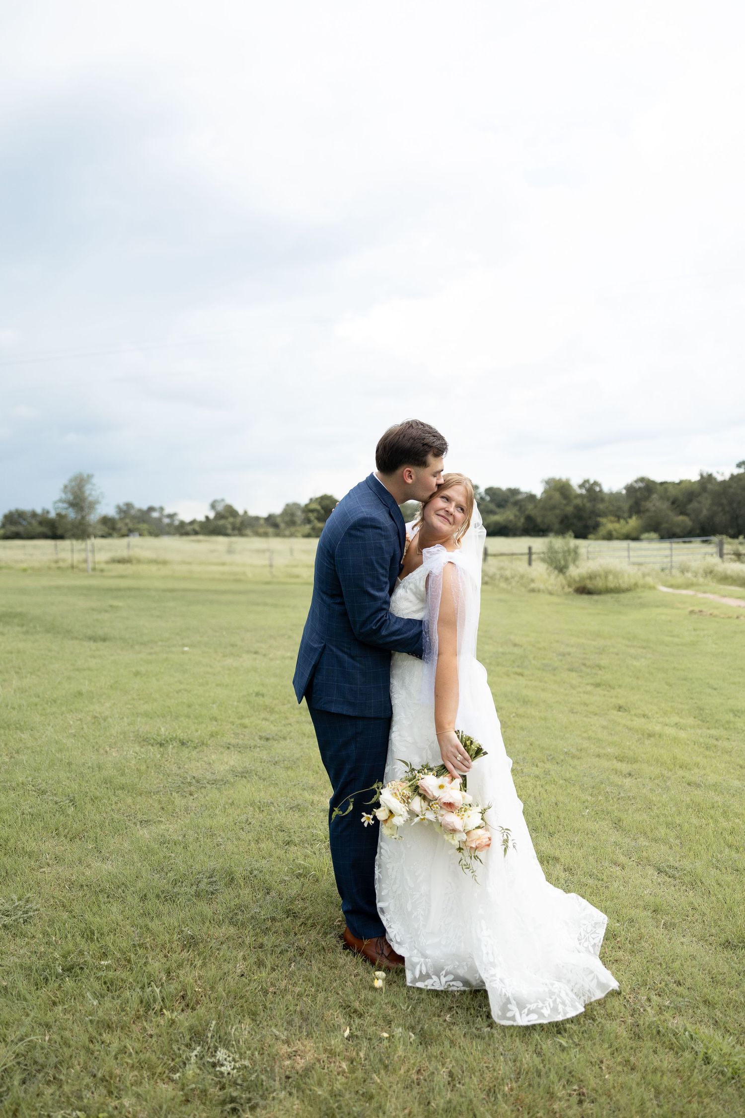 Wedding couple embraces in a serene green field setting.