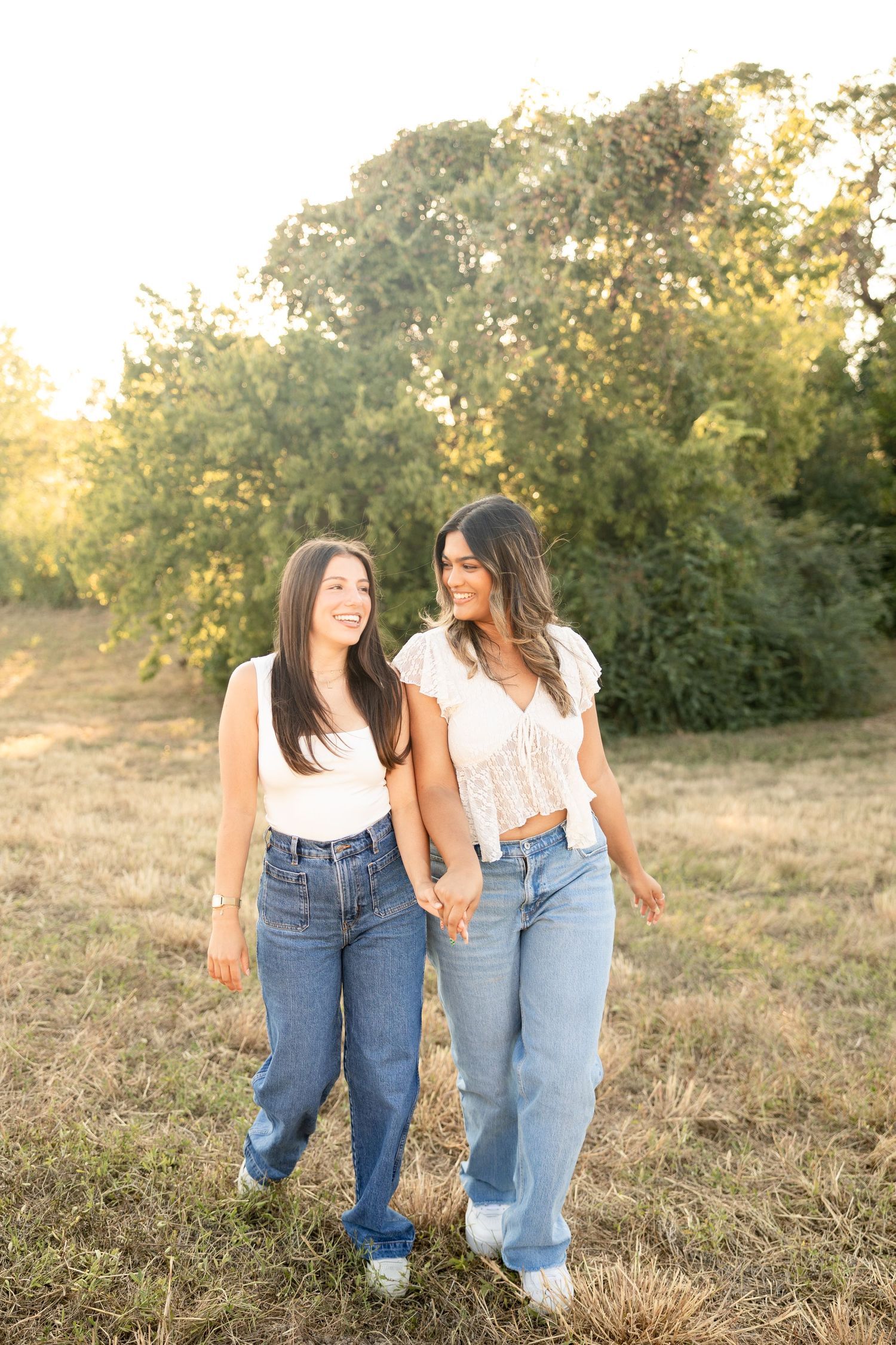 Two friends in denim jeans walking together through a sunlit field.