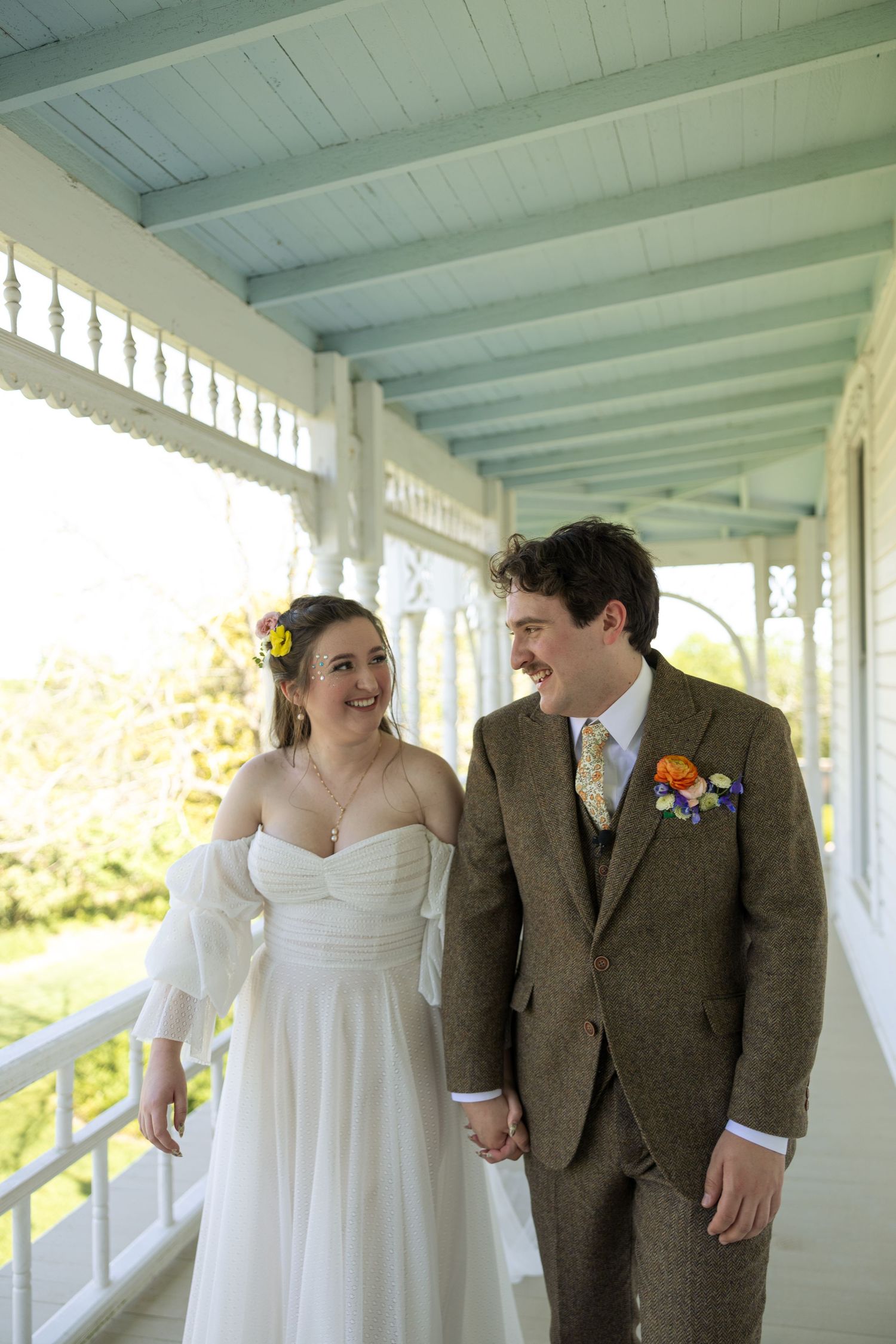 Wedding couple shares candid moments while walking along a covered porch.
