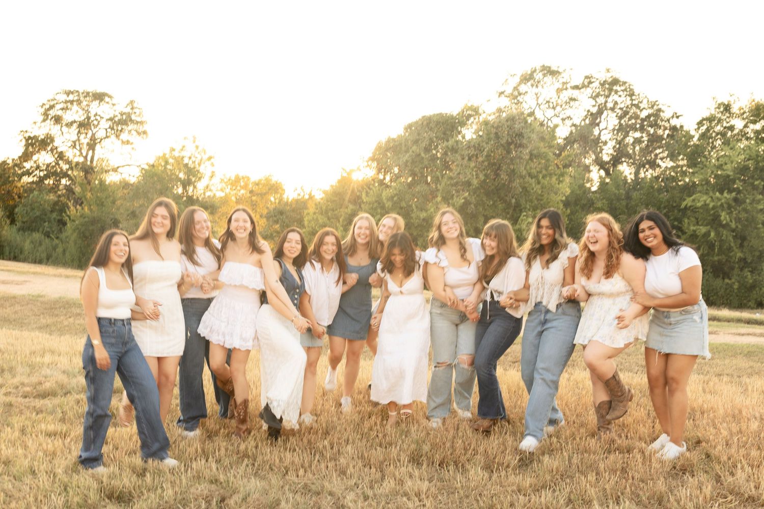 Friends wearing white and blue outfits posing together in a field during golden hour.