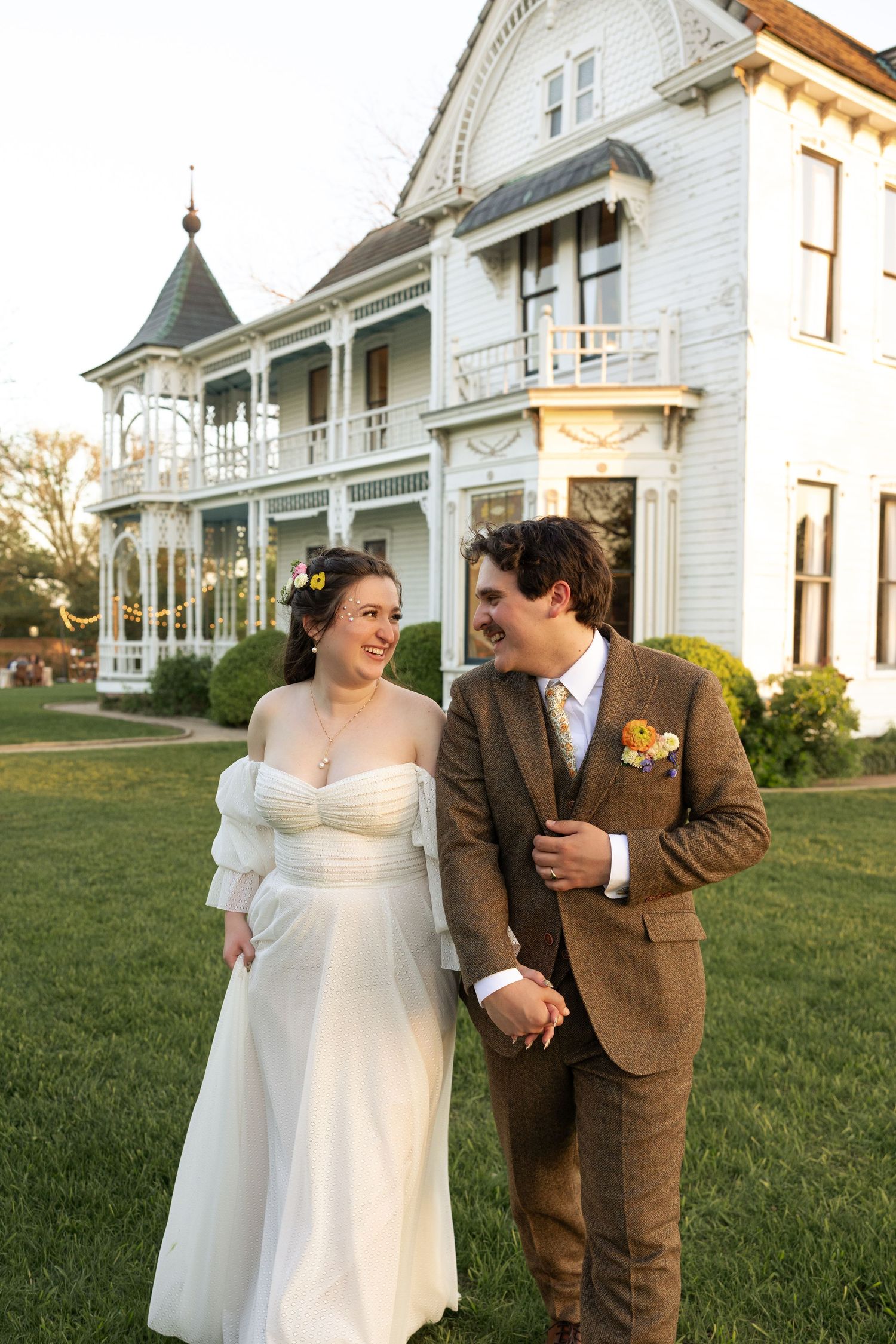 A couple shares a joyful moment on their wedding day in front of white Victorian houses.