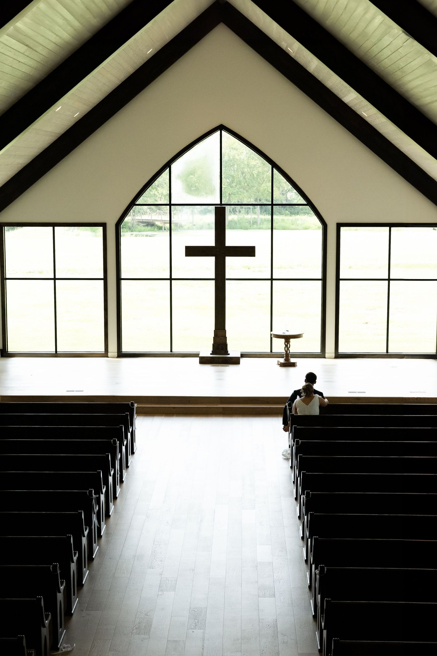 Empty modern church interior with wooden pews and large windows.