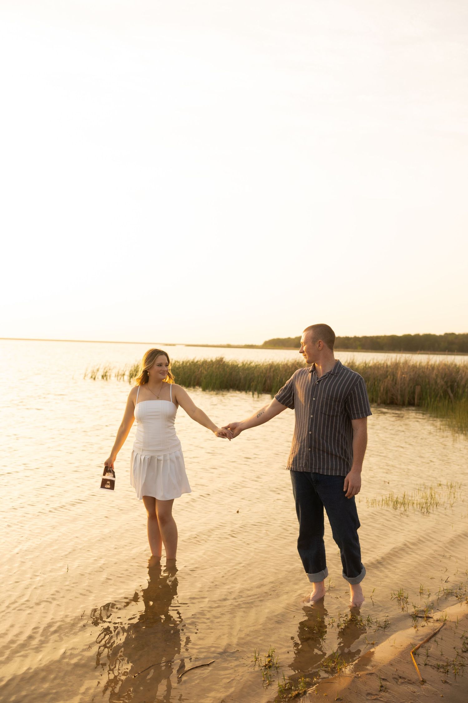 Couple walking along beach shoreline during golden hour sunset.
