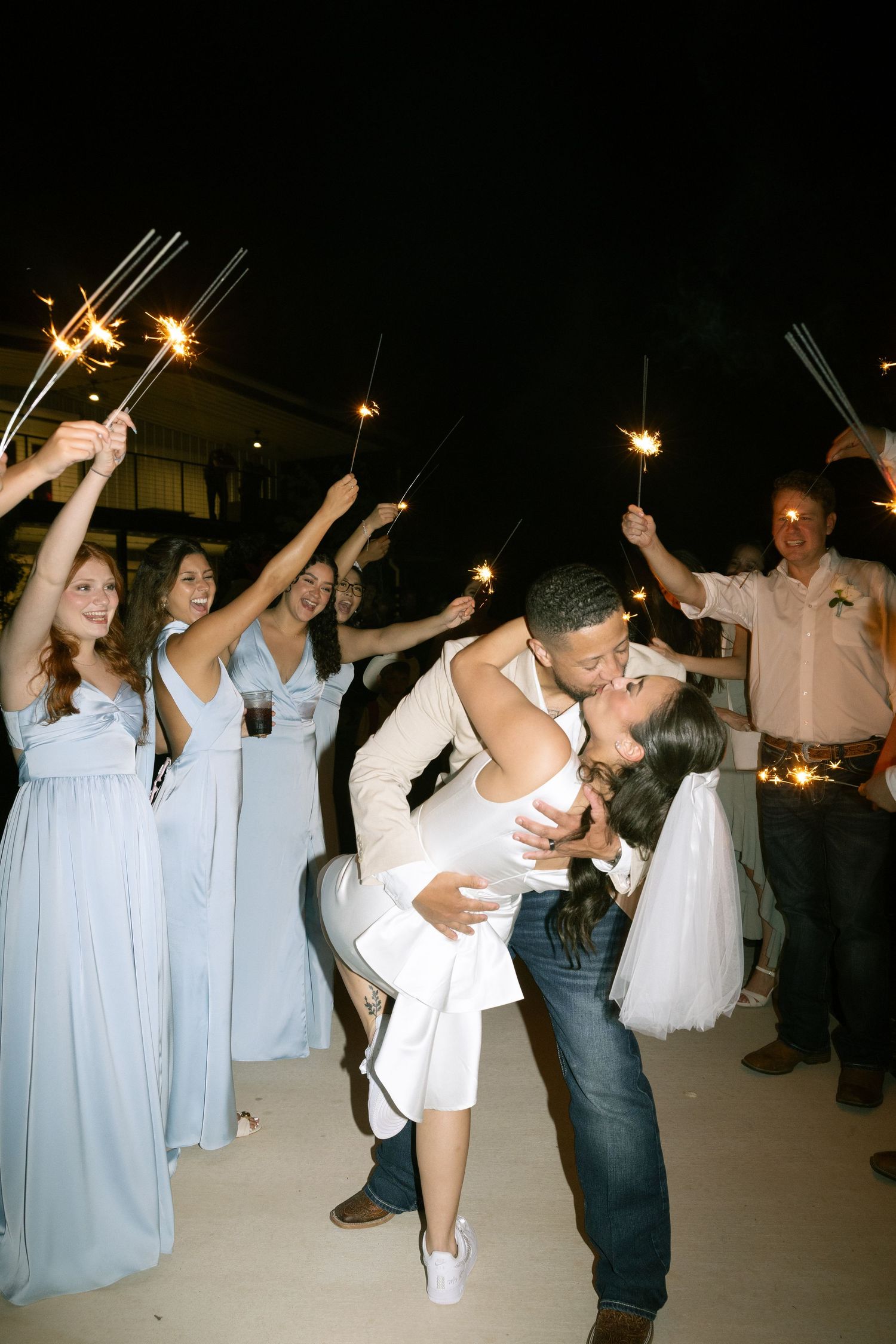 Wedding celebration at night with guests holding sparklers and dancing under the stars.