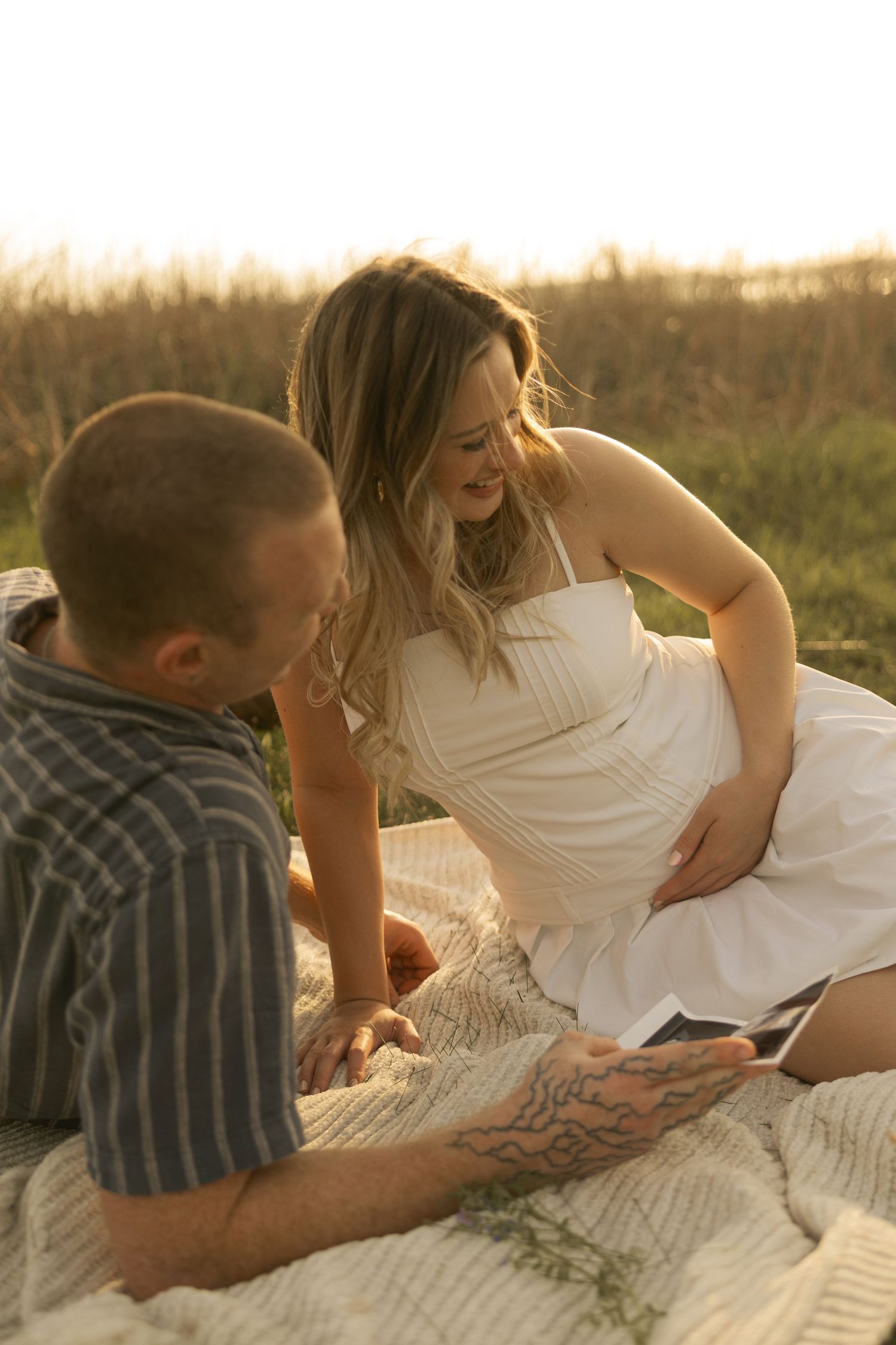 Couple lying on blanket at beach during golden hour photo session.