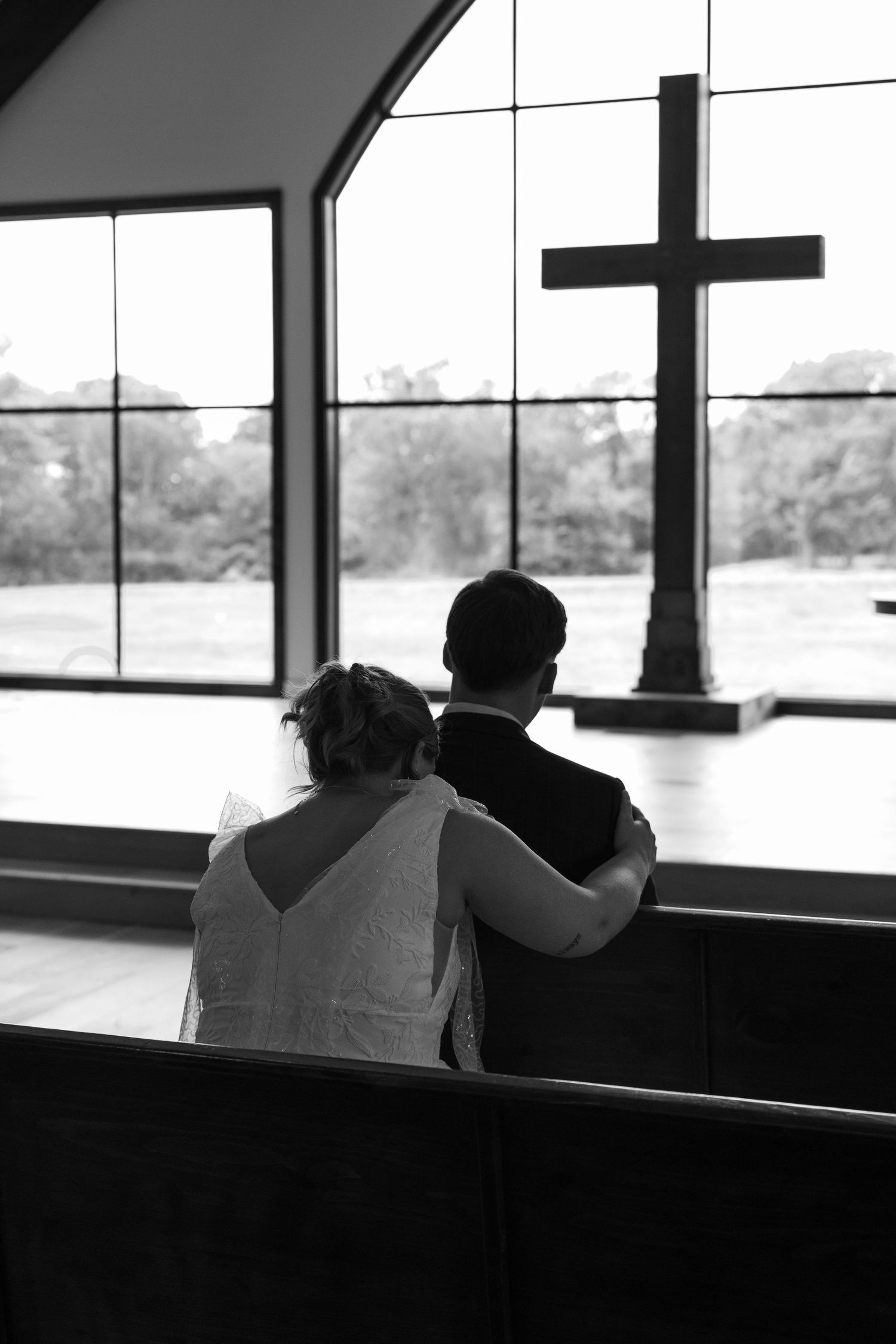 Silhouettes of a couple sitting together near large windows in a church.