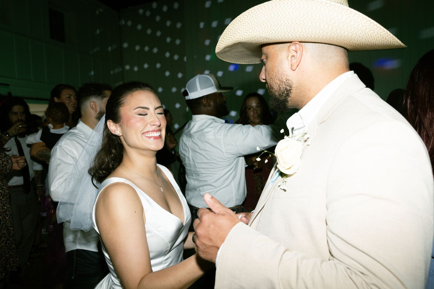 A couple dances together at their wedding reception with the groom wearing a white cowboy hat.