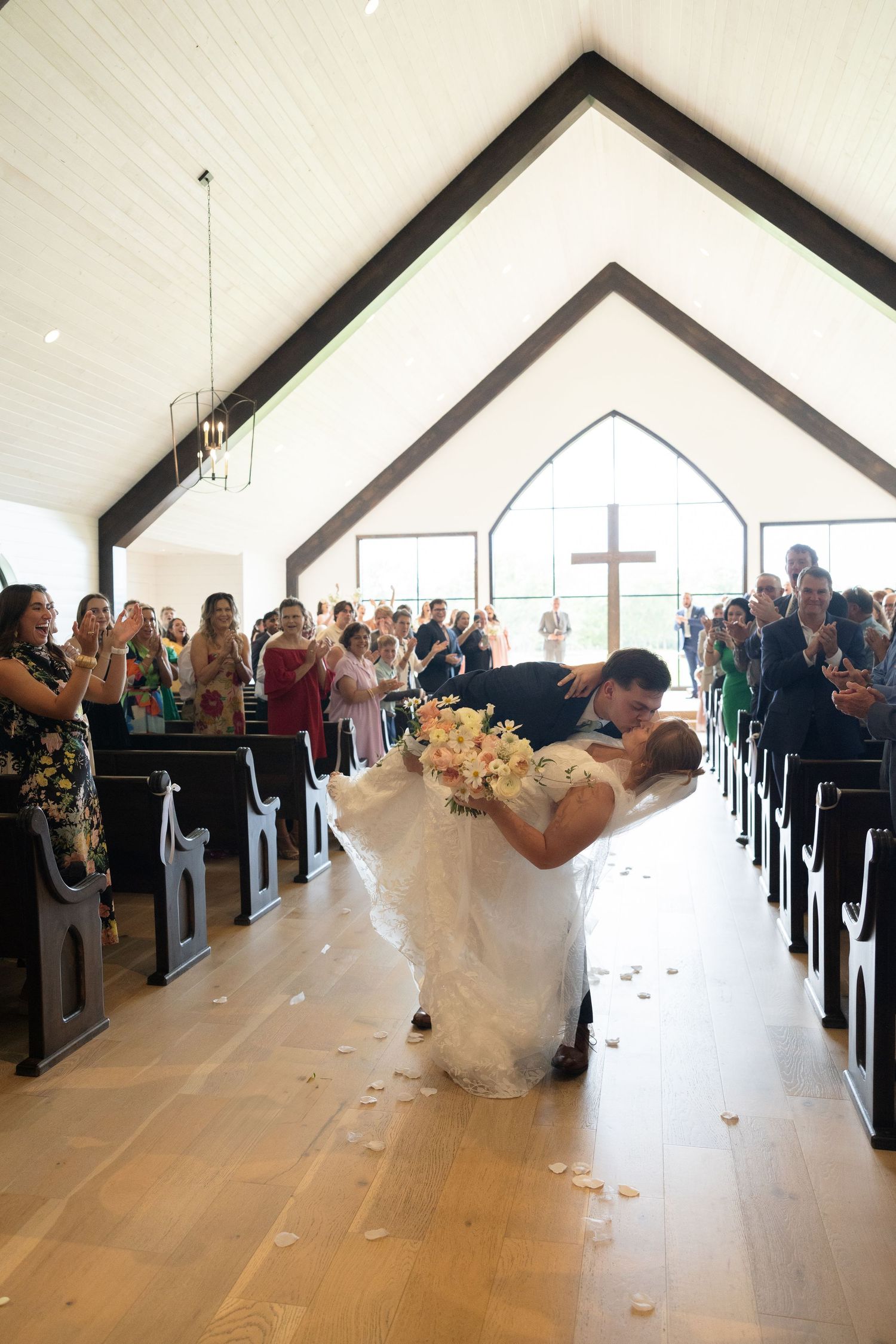 Wedding ceremony in progress inside bright modern chapel with guests in attendance.