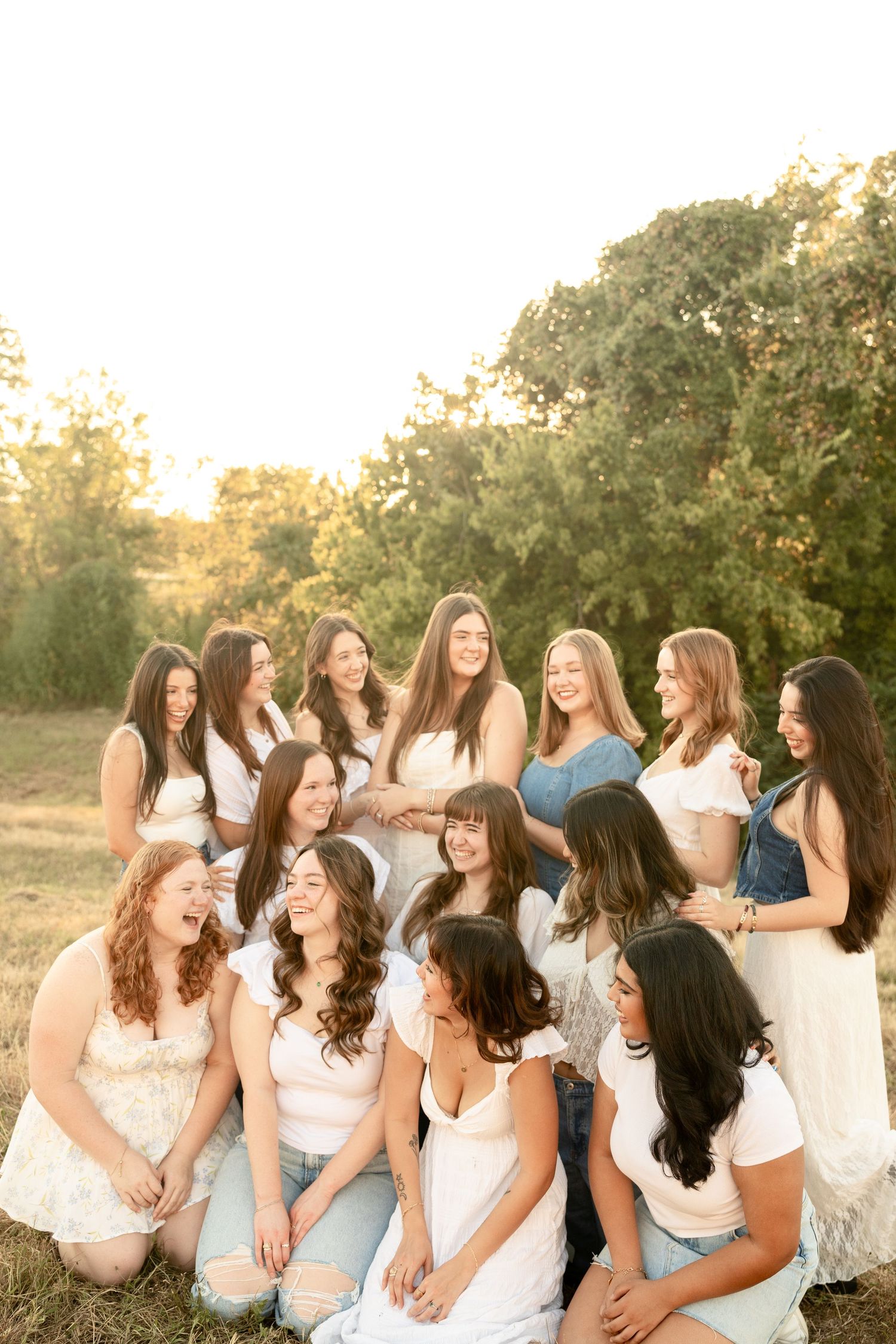 Group portrait of friends in white and denim clothing sitting together outdoors.