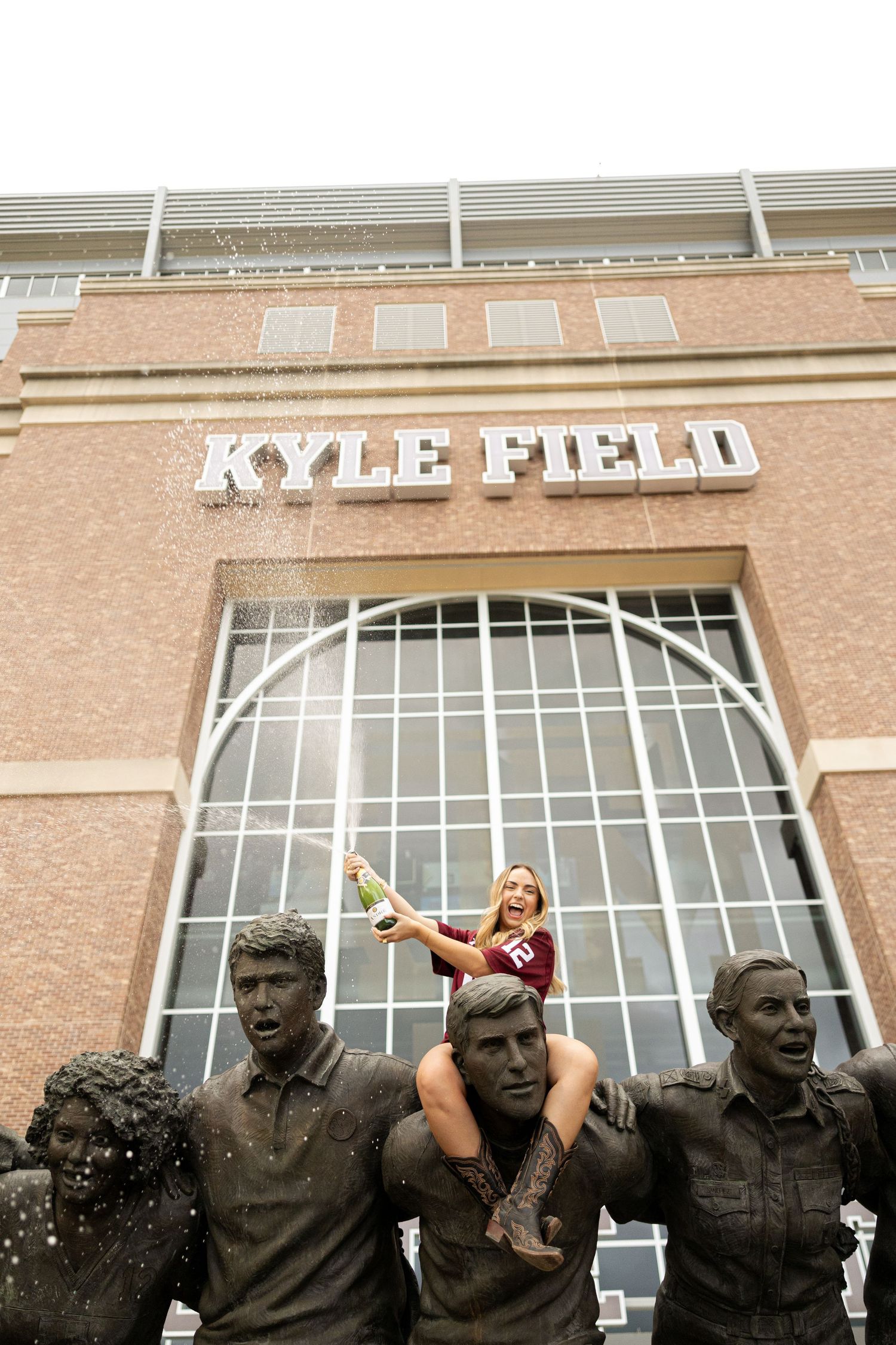 Graduate poses on Kyle Field statues at Texas A&M University during photo session.