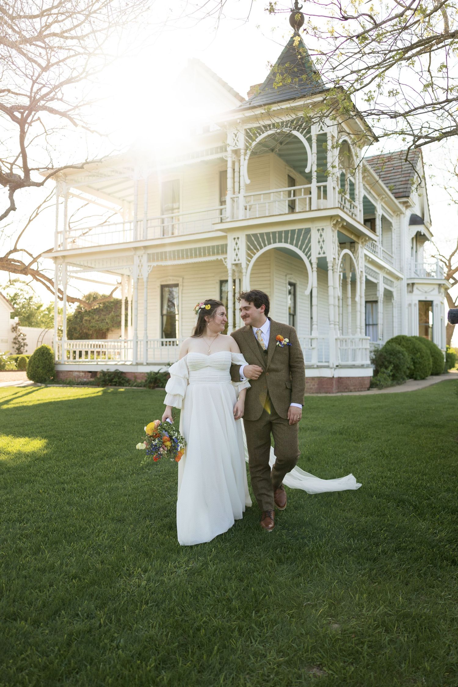 A wedding photo in front of a stunning Victorian mansion with white trim and ornate details.