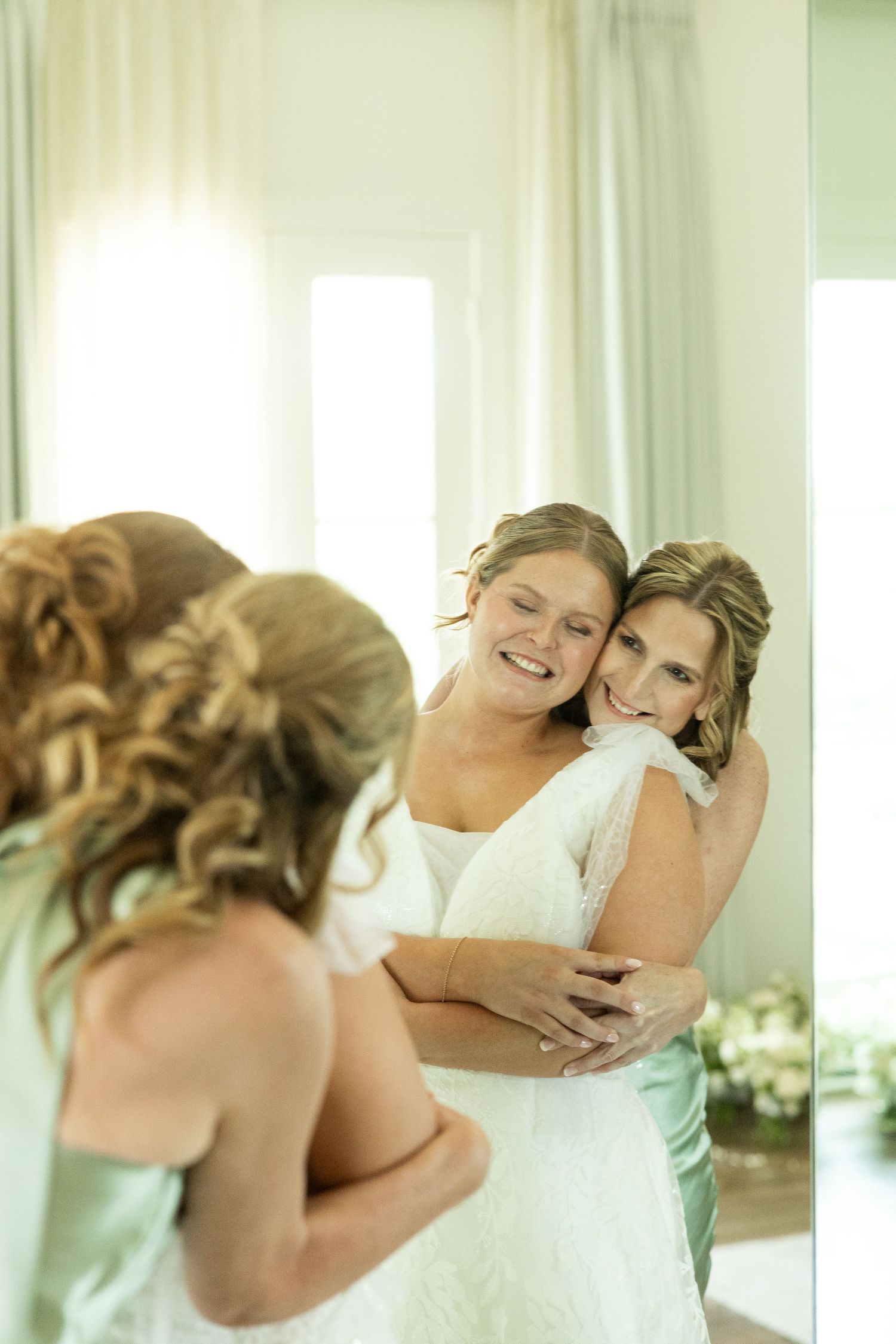 Friends share emotional embrace in sunlit room with flowing curtains.