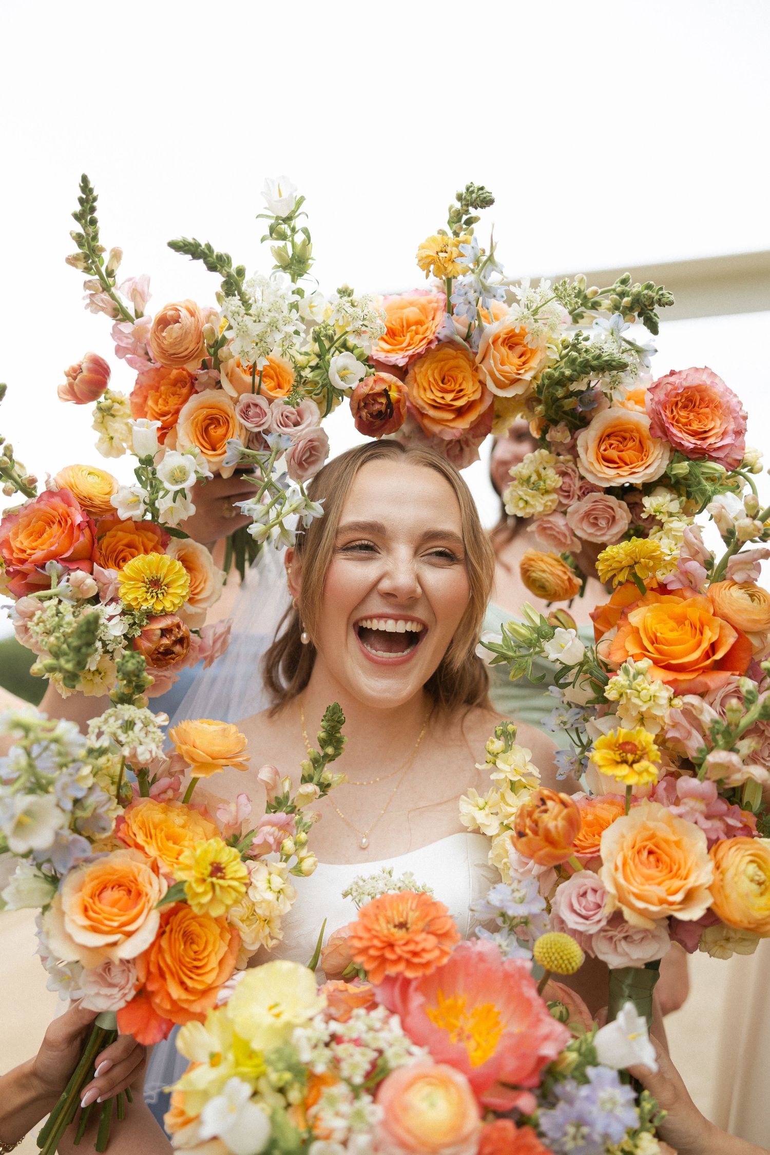 Laughing bride surrounded by a circular frame of colorful orange, pink, and yellow flowers on her wedding day.