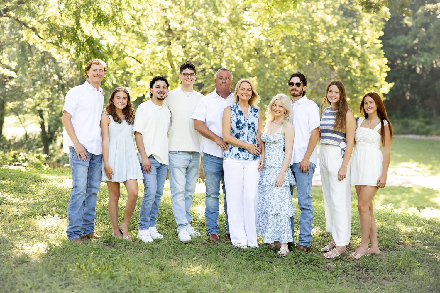 A group in coordinated white and denim outfits poses casually outdoors in a grassy park setting.
