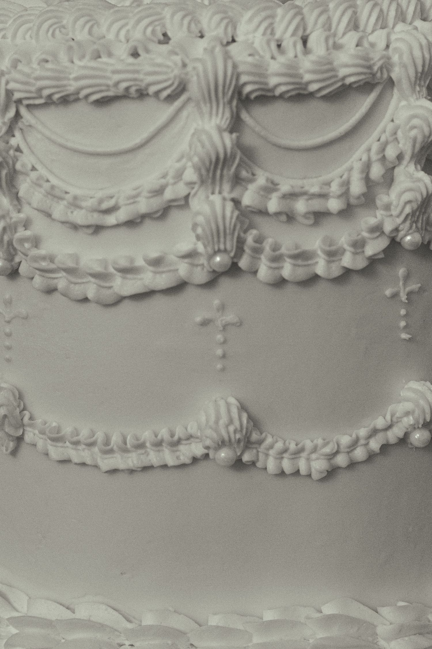 Detailed white frosting decorations on a wedding cake featuring intricate piped swags and crosses.