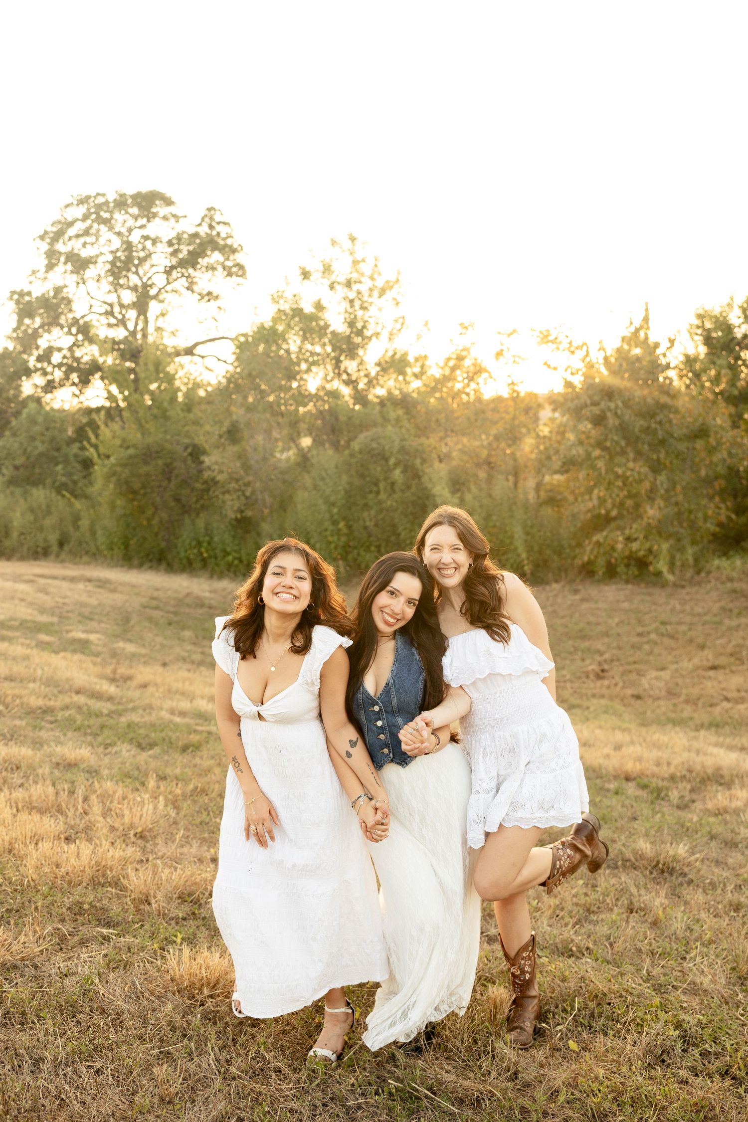Friends laughing and holding hands while walking through a sunny field.
