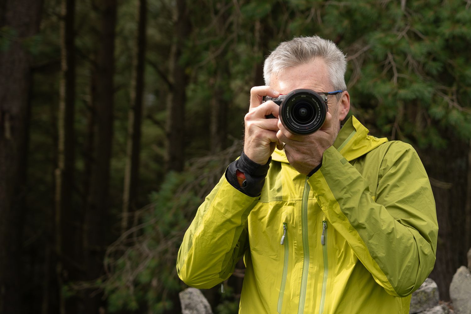Person in yellow raincoat photographing in dark forest environment.