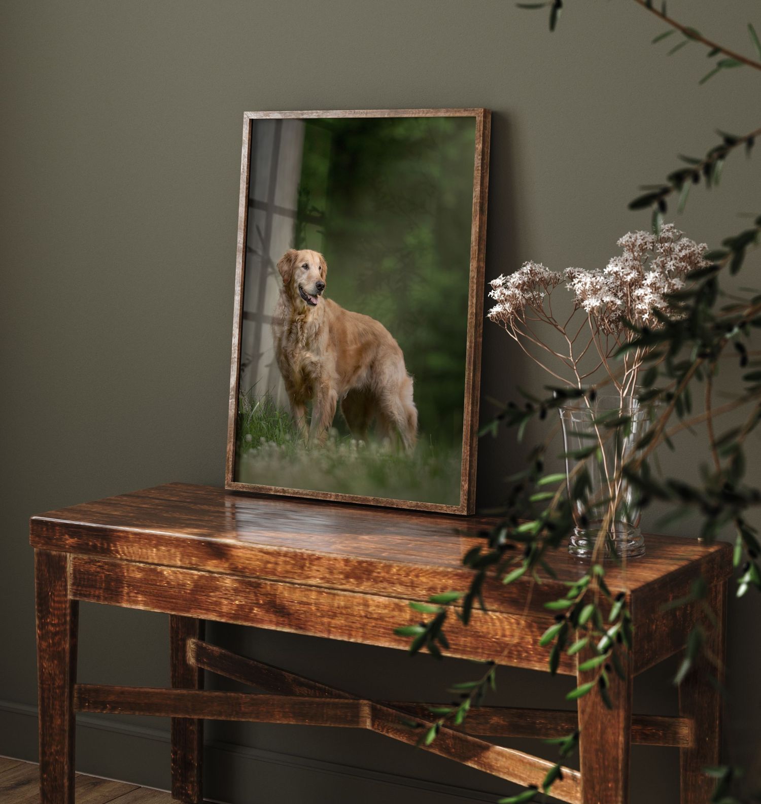 Rustic wooden desk with a framed artwork and leafy plant decor creates an elegant workspace setting against a green wall.