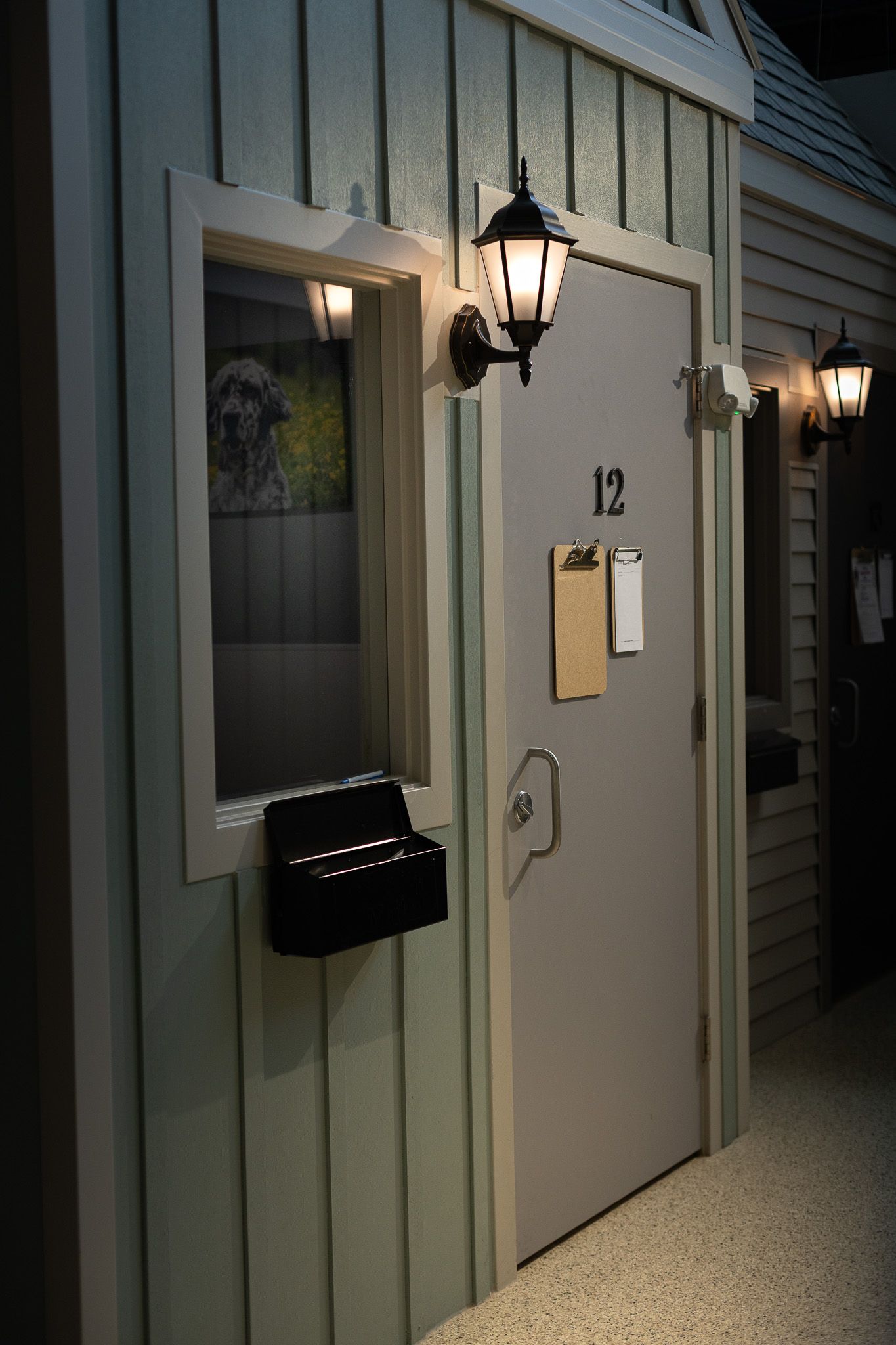 Indoor kennel suite number 12 with green walls, wall lanterns, window, clipboard, and black metal mailbox.