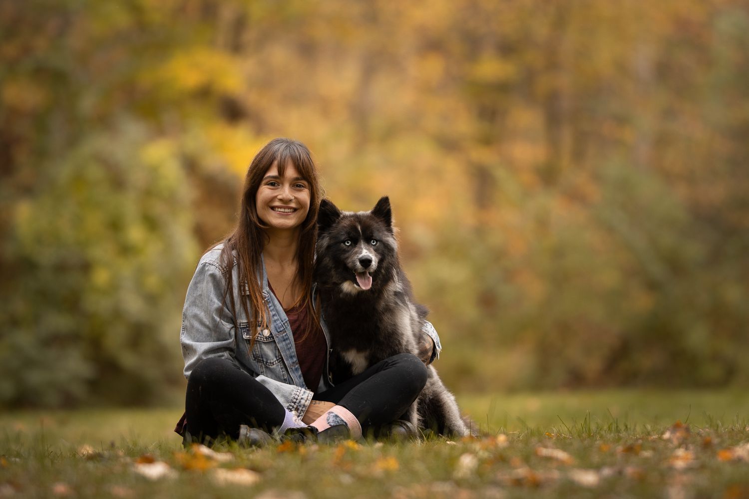 A person and their black dog enjoy a cozy autumn day together in a park with fallen leaves.