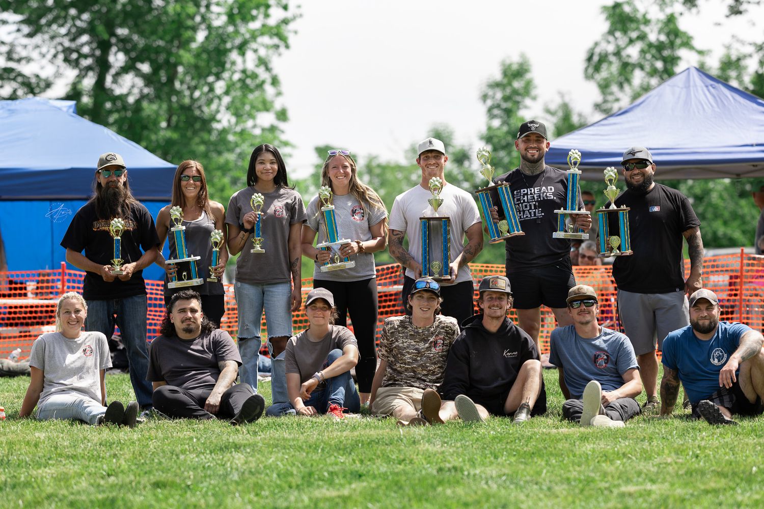 Group of trophy winners posing outdoors at a disc golf tournament on a sunny day in a green park.