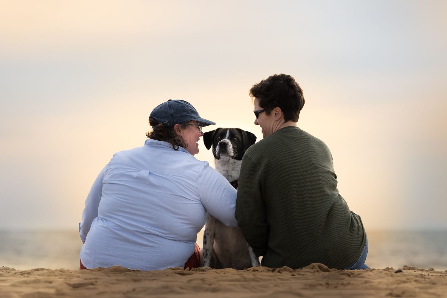 Two people sit close together on a beach watching a sunset over the ocean horizon.