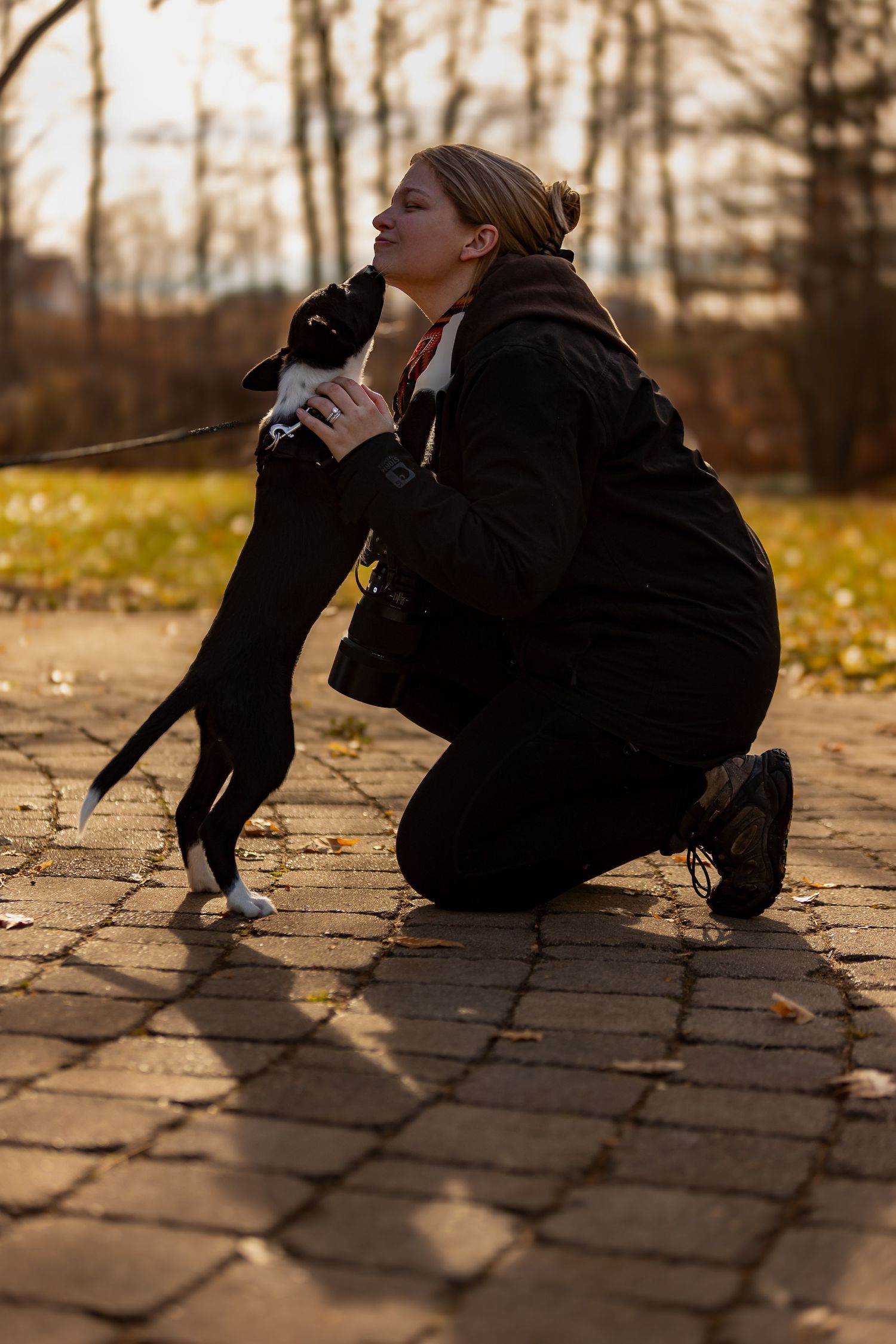A person in black clothing crouches low on brick pavement during an autumn sunset.