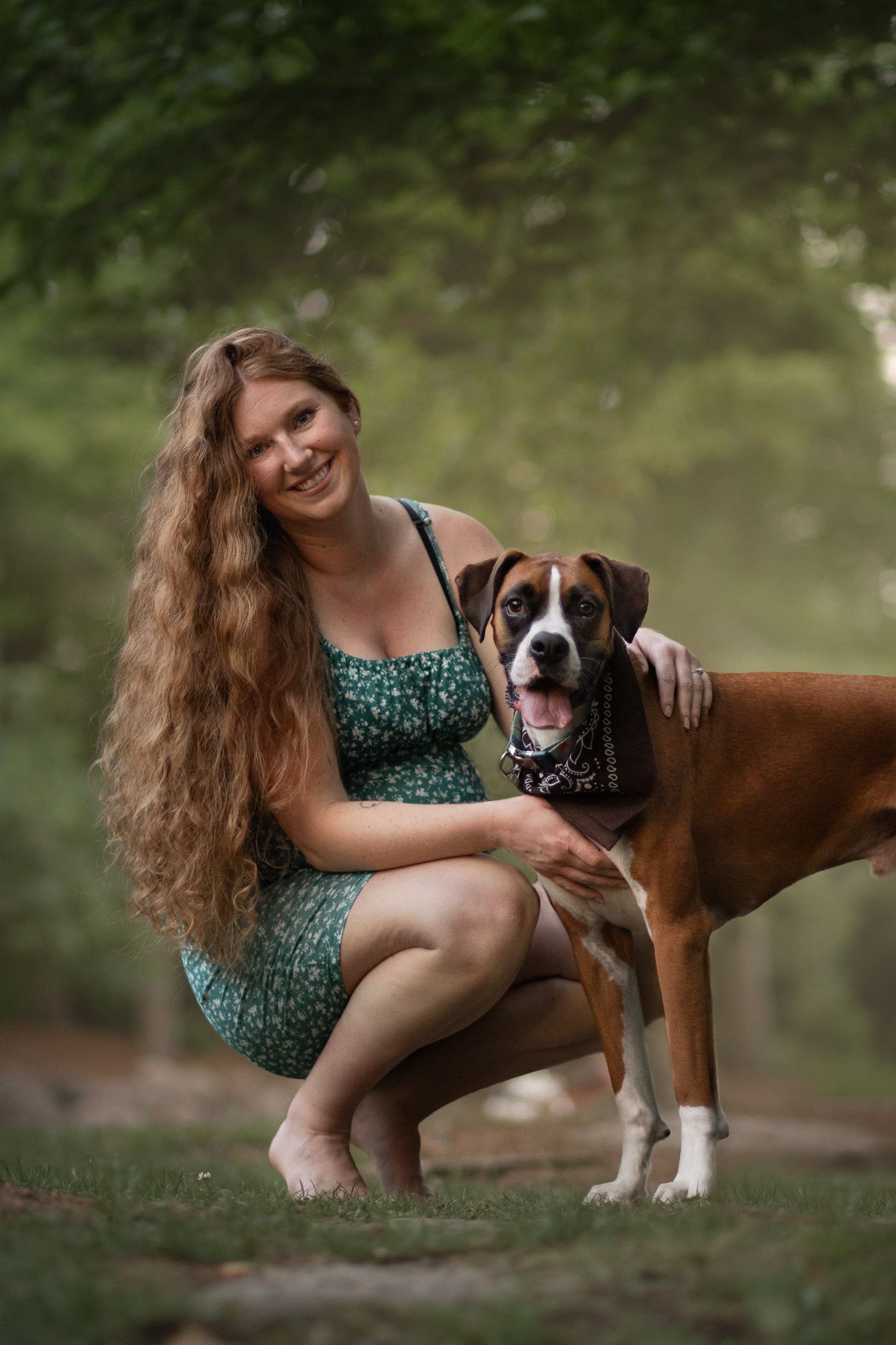 A boxer dog and someone in a green dress pose together on grass during a summer photoshoot.