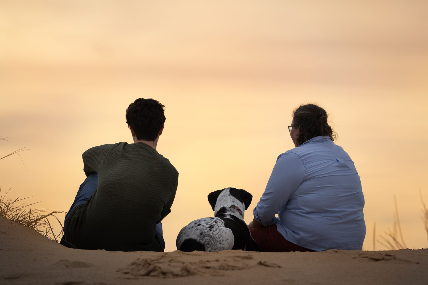 Three silhouettes sit together watching a golden sunset over a scenic horizon.