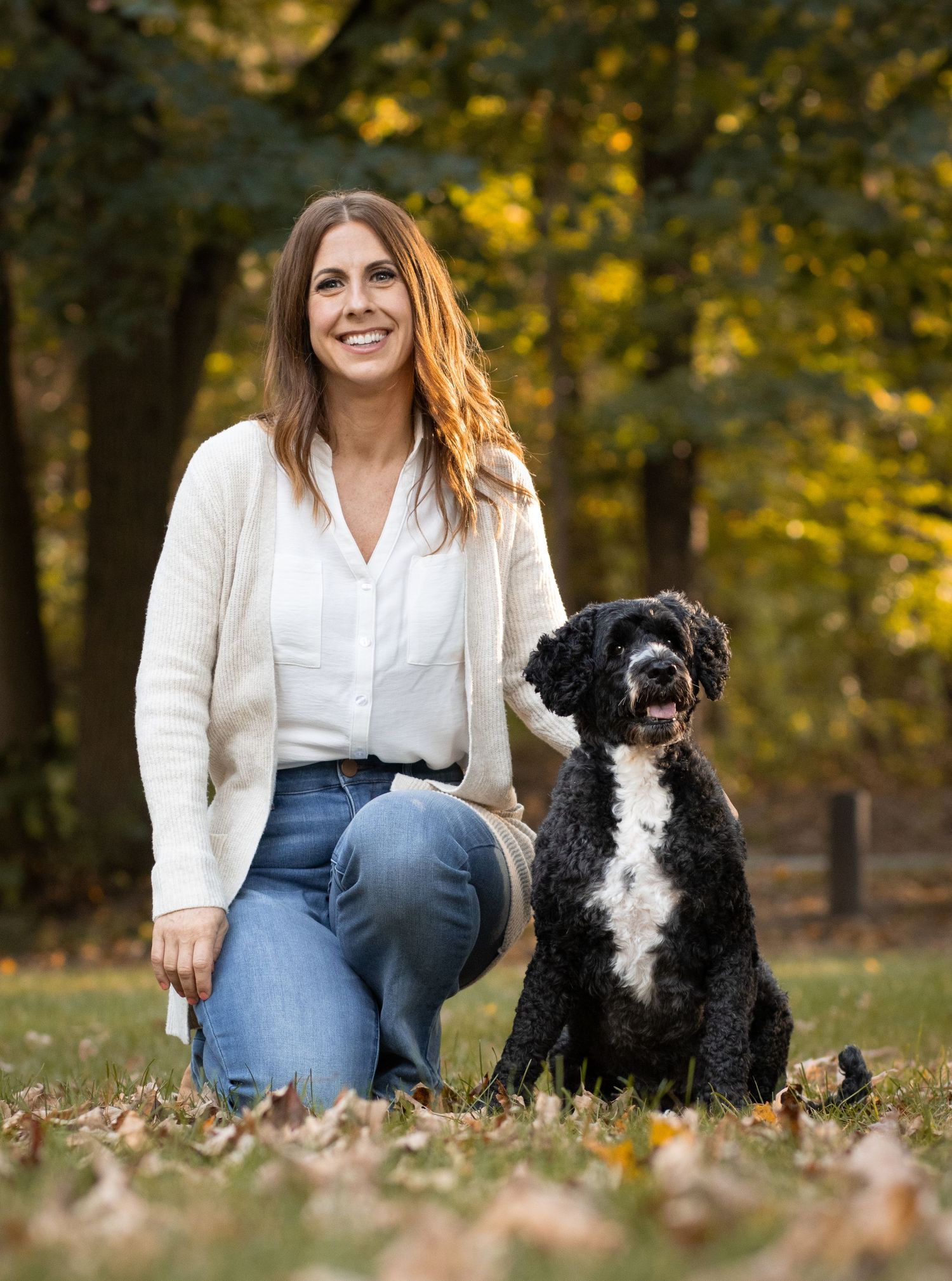 Black and white Portuguese Water Dog sitting next to person in autumn park setting.
