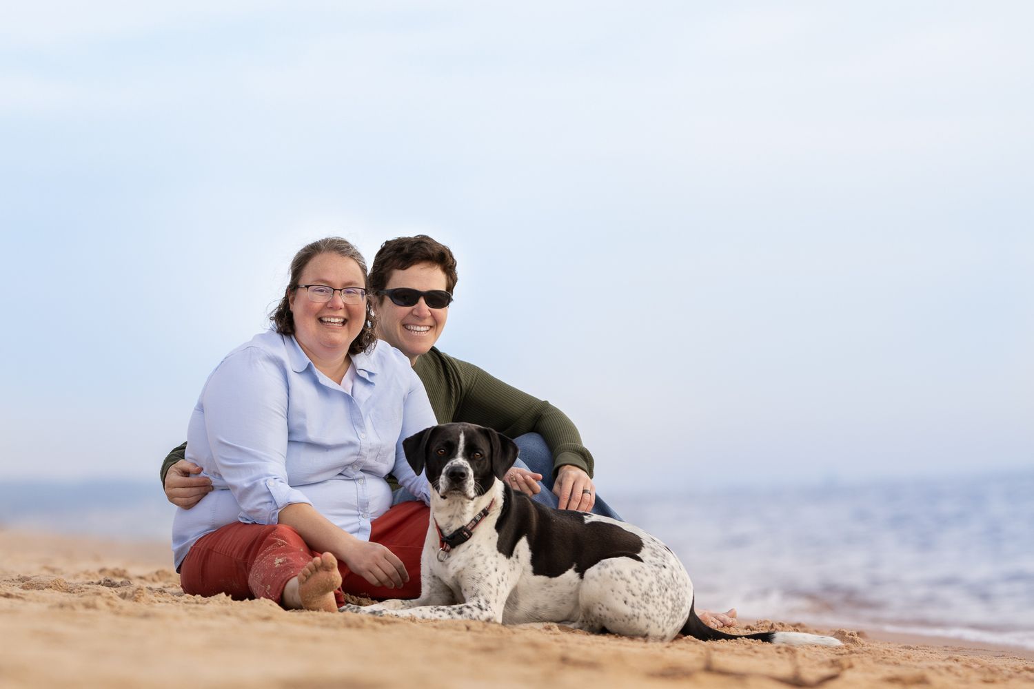 People and a dog relaxing together on a sandy beach with ocean waves in the background.