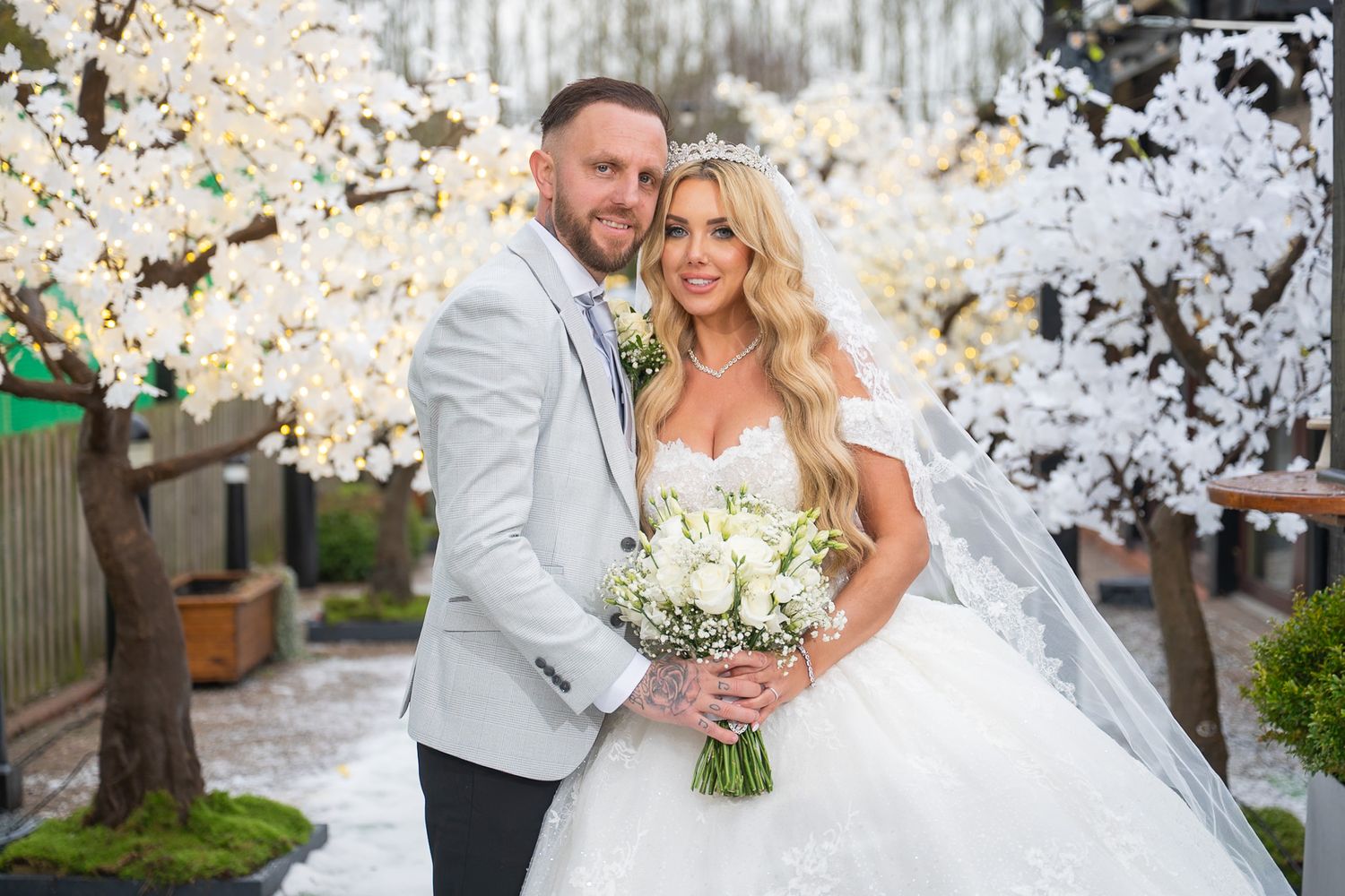 A couple poses together under blooming cherry blossom trees during a spring wedding celebration.