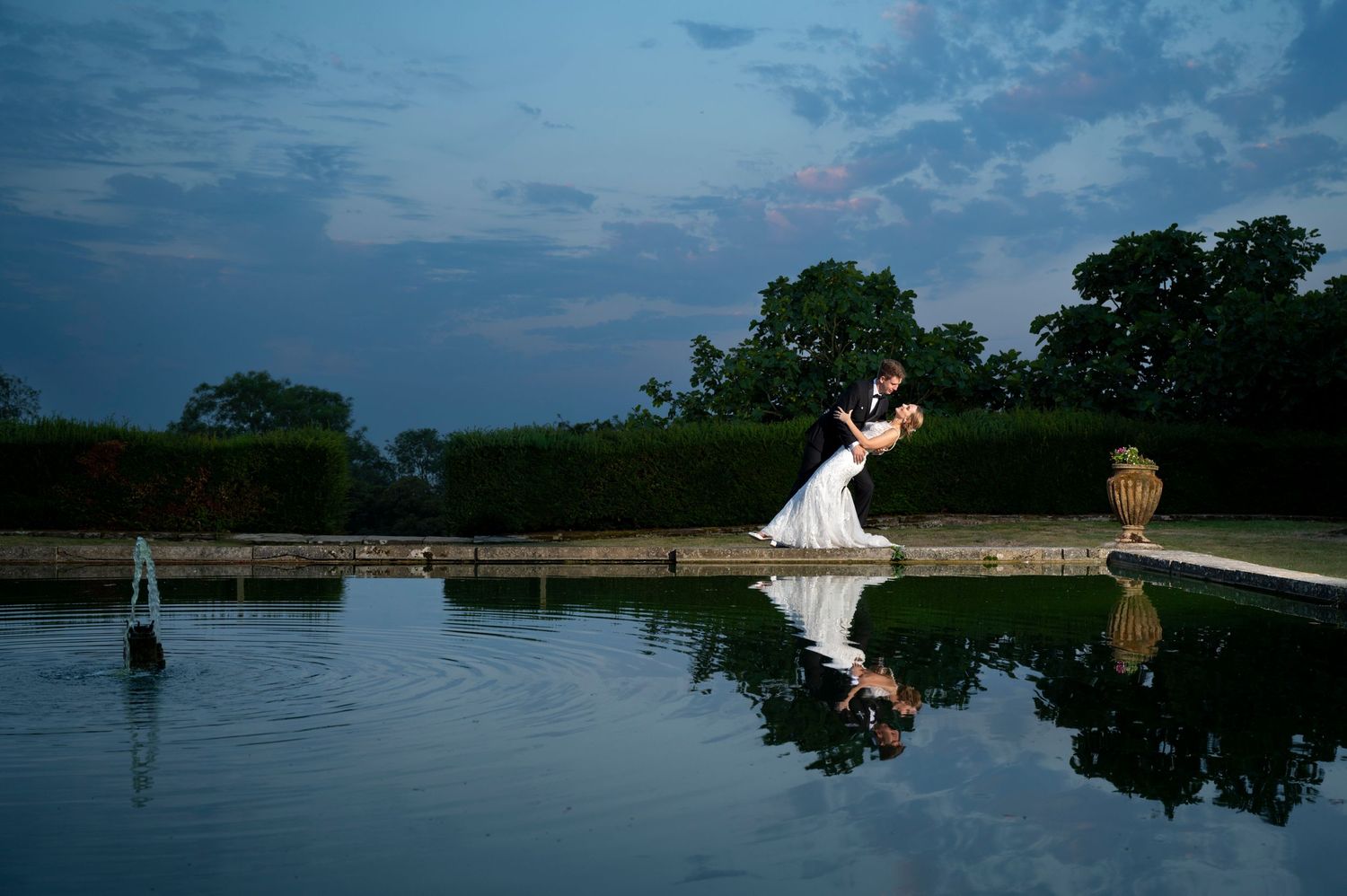 A Fine art posed photo of a couple as the groom and his bride do a Hollywood Dip. Their reflection caught in the pool of water.