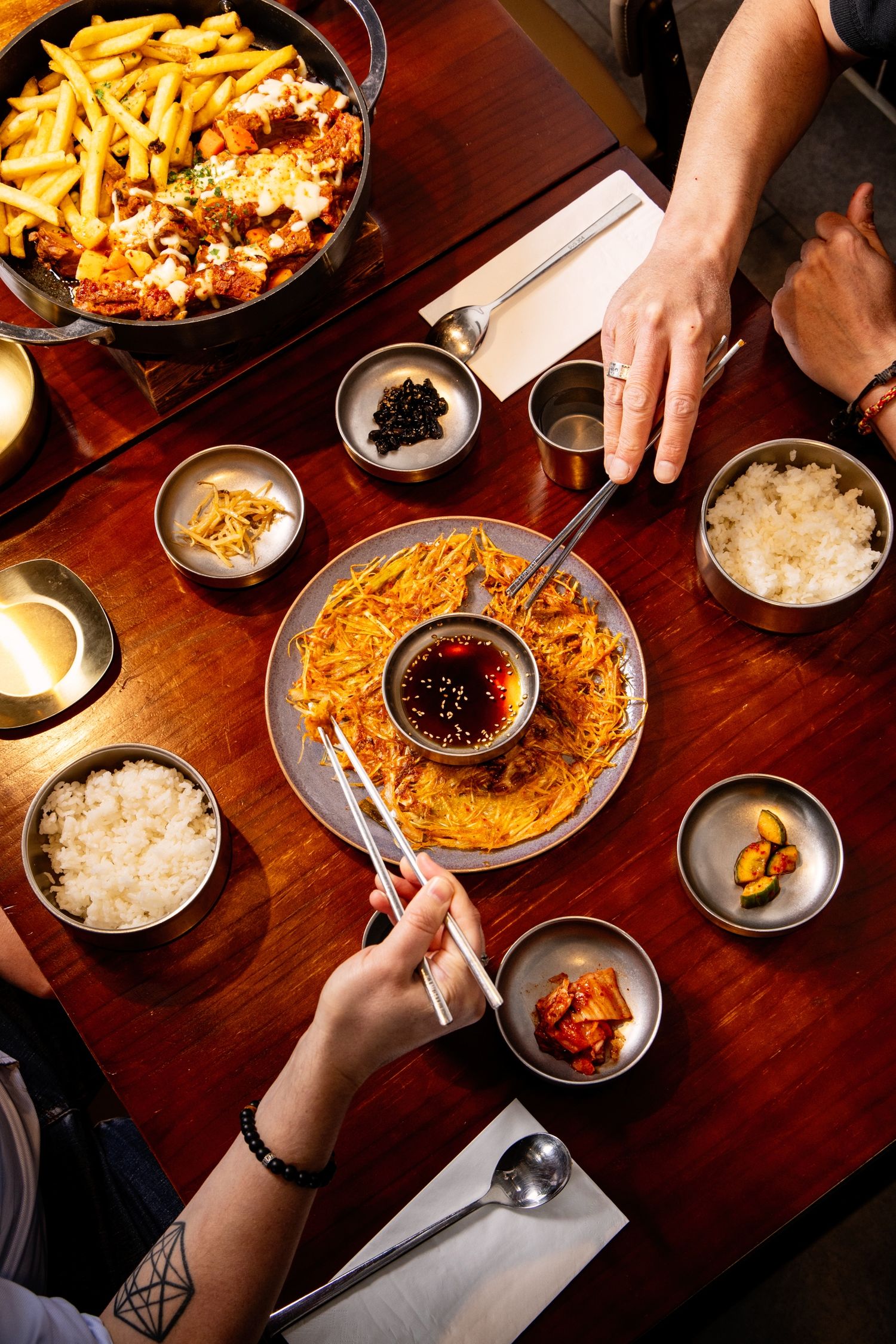 Overhead view of Korean dining table with banchan, rice, chopsticks, and shared dishes.