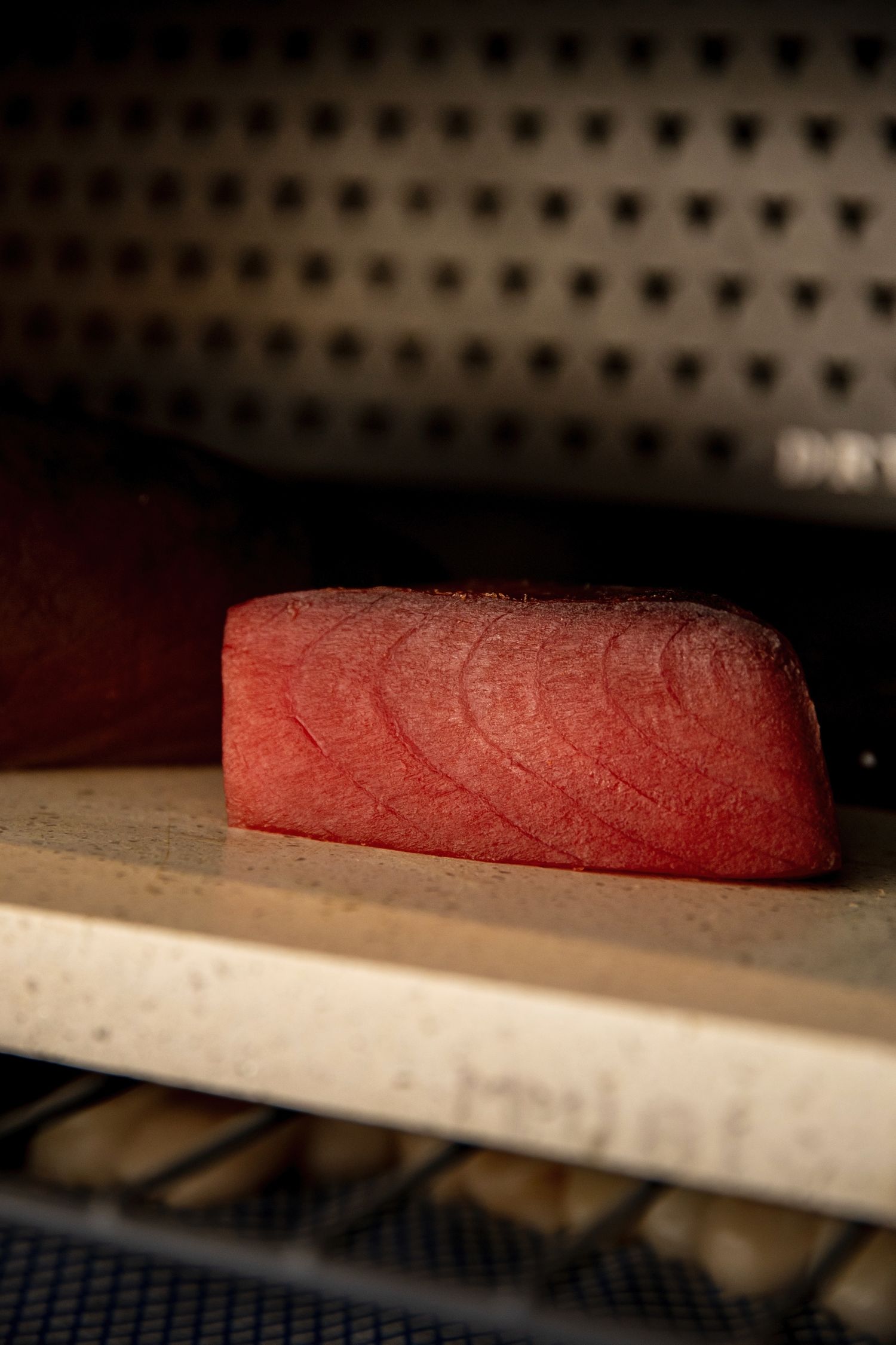 A raw tuna steak with visible marbling sits on a wooden cutting board under dim lighting.
