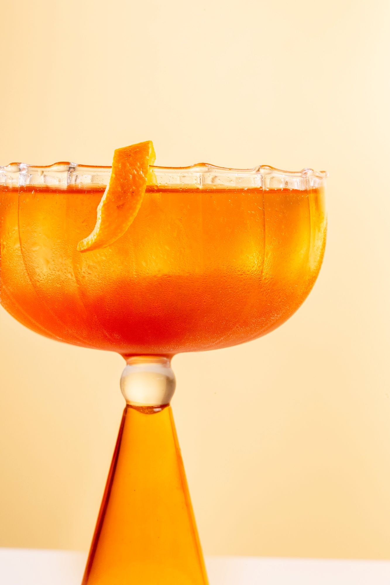 Four champagne coupes filled with bright orange cocktails against a peach-colored background create an elegant display.