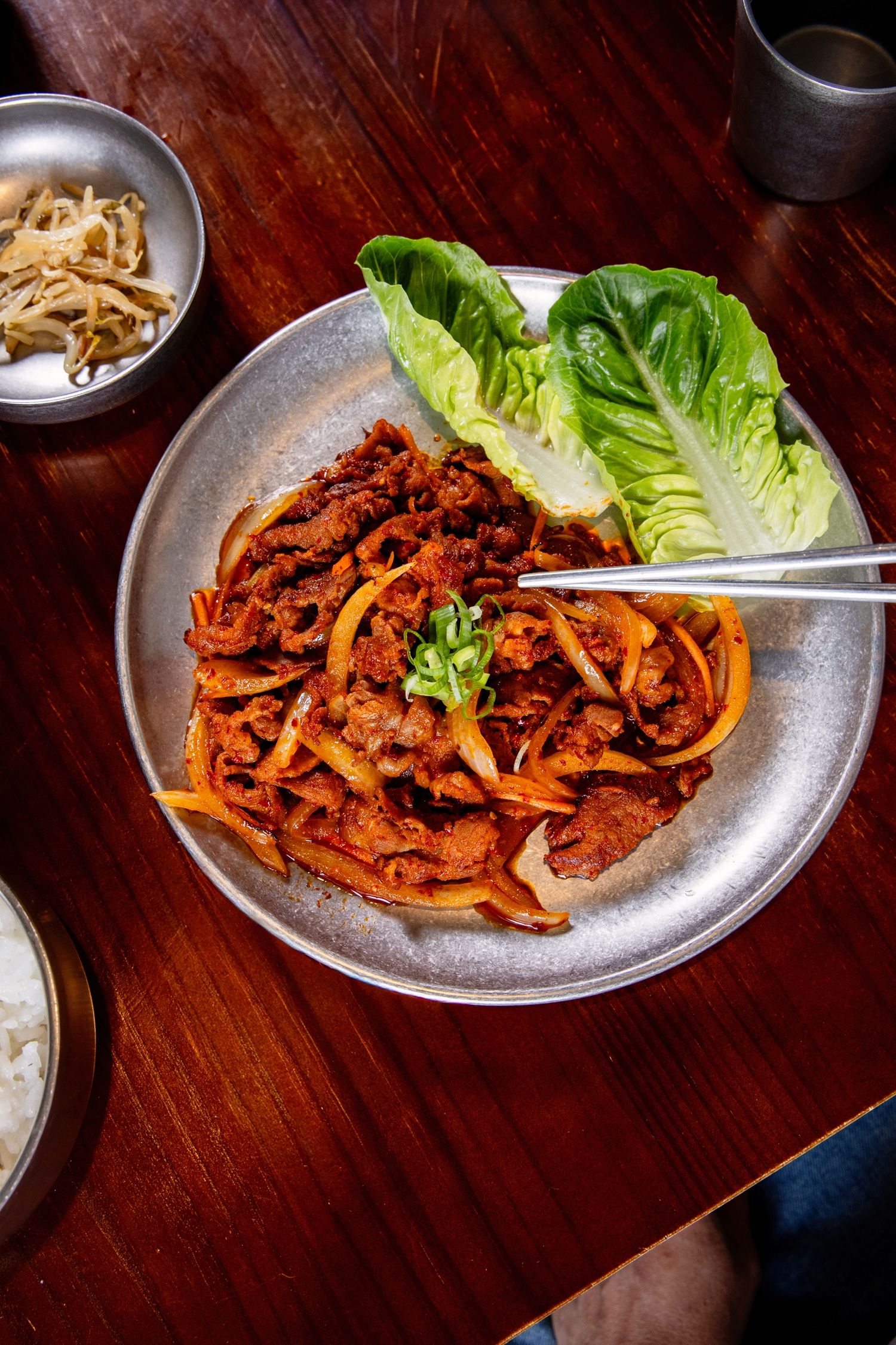 Korean spicy stir-fried pork bulgogi served on metal plate with fresh lettuce and chopsticks.