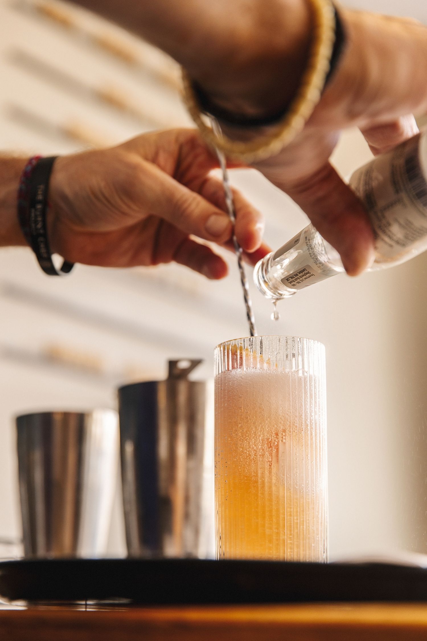 Hands pouring and straining cocktail ingredients between metal shakers in sequence showing mixology technique.