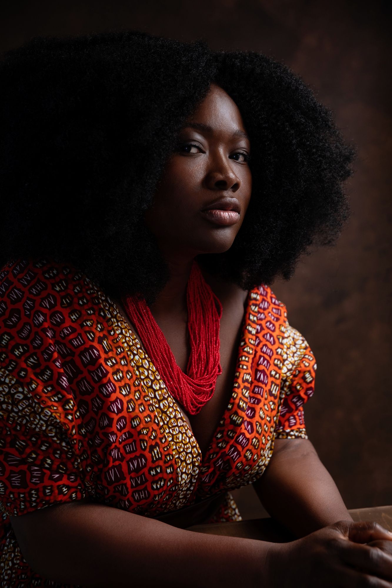 Portrait of a woman with natural afro hair wearing vibrant red and orange patterned clothing.