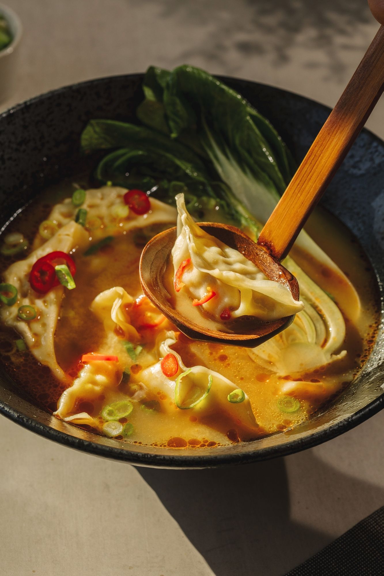 Asian soup with gyoza, bok choy and chilis, being served with wooden spoon.
