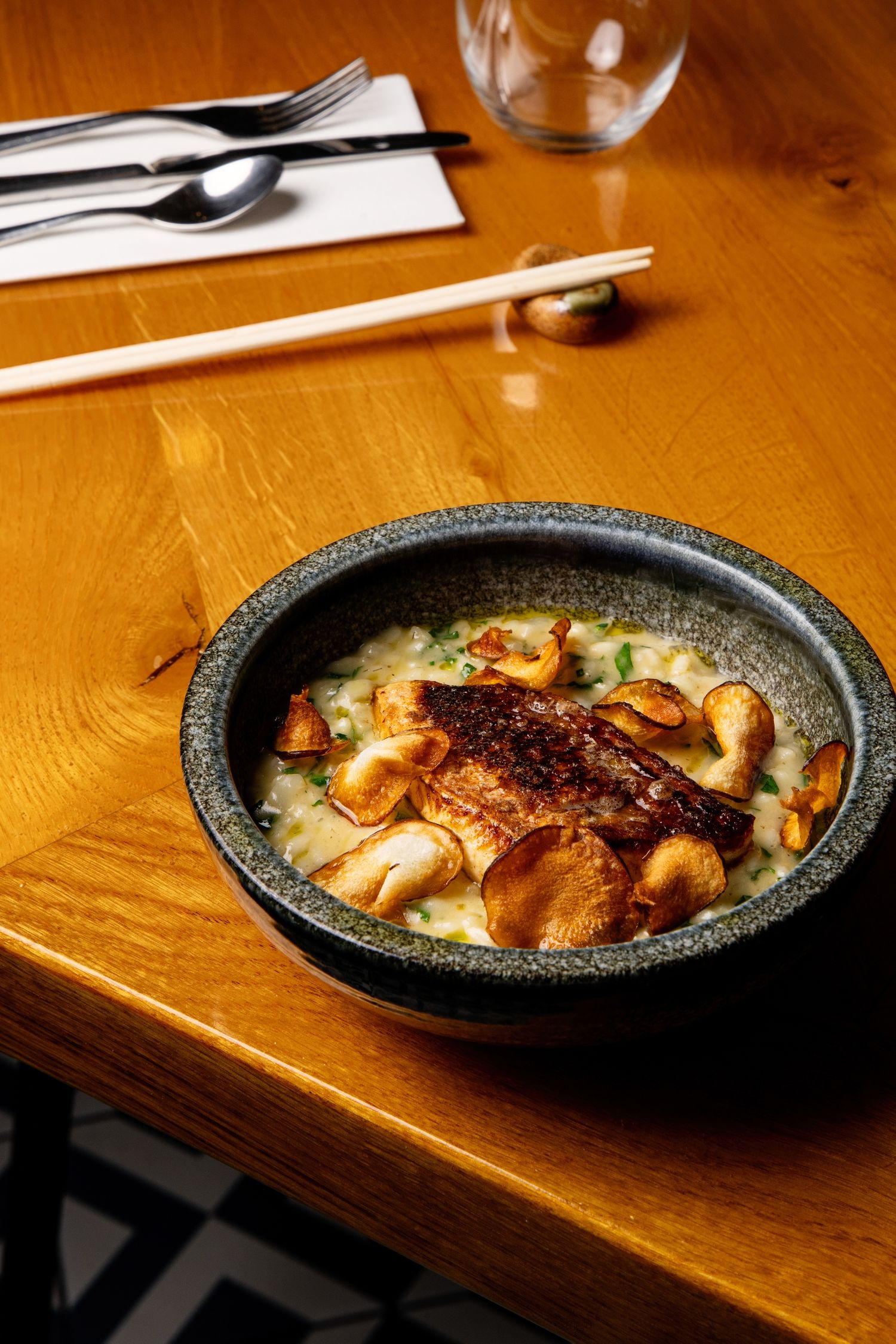 Asian-style seafood soup with grilled fish and mushrooms served in a black stone bowl on wooden table.