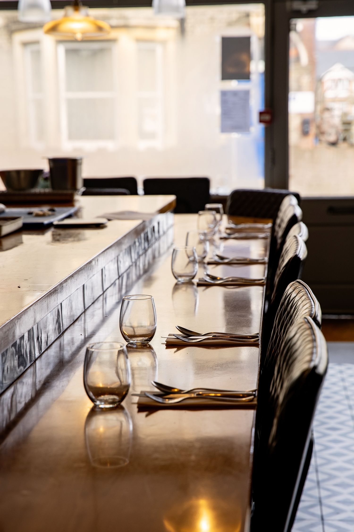 Restaurant bar counter with elegant place settings featuring wine glasses and utensils on a dark wooden surface.