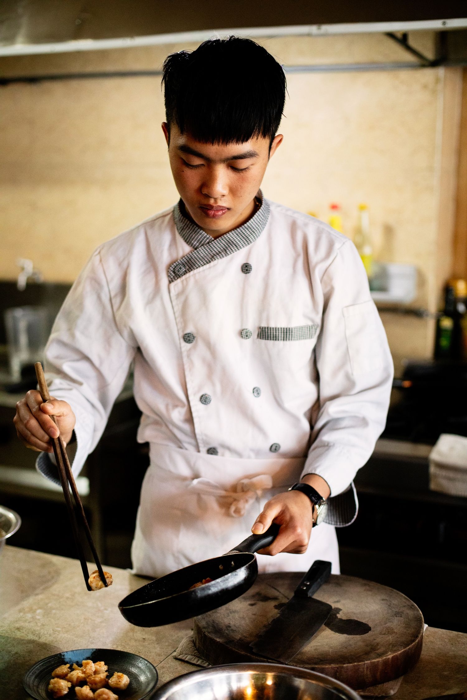 Chef in white uniform carefully prepares dishes using traditional cooking techniques in restaurant kitchen.