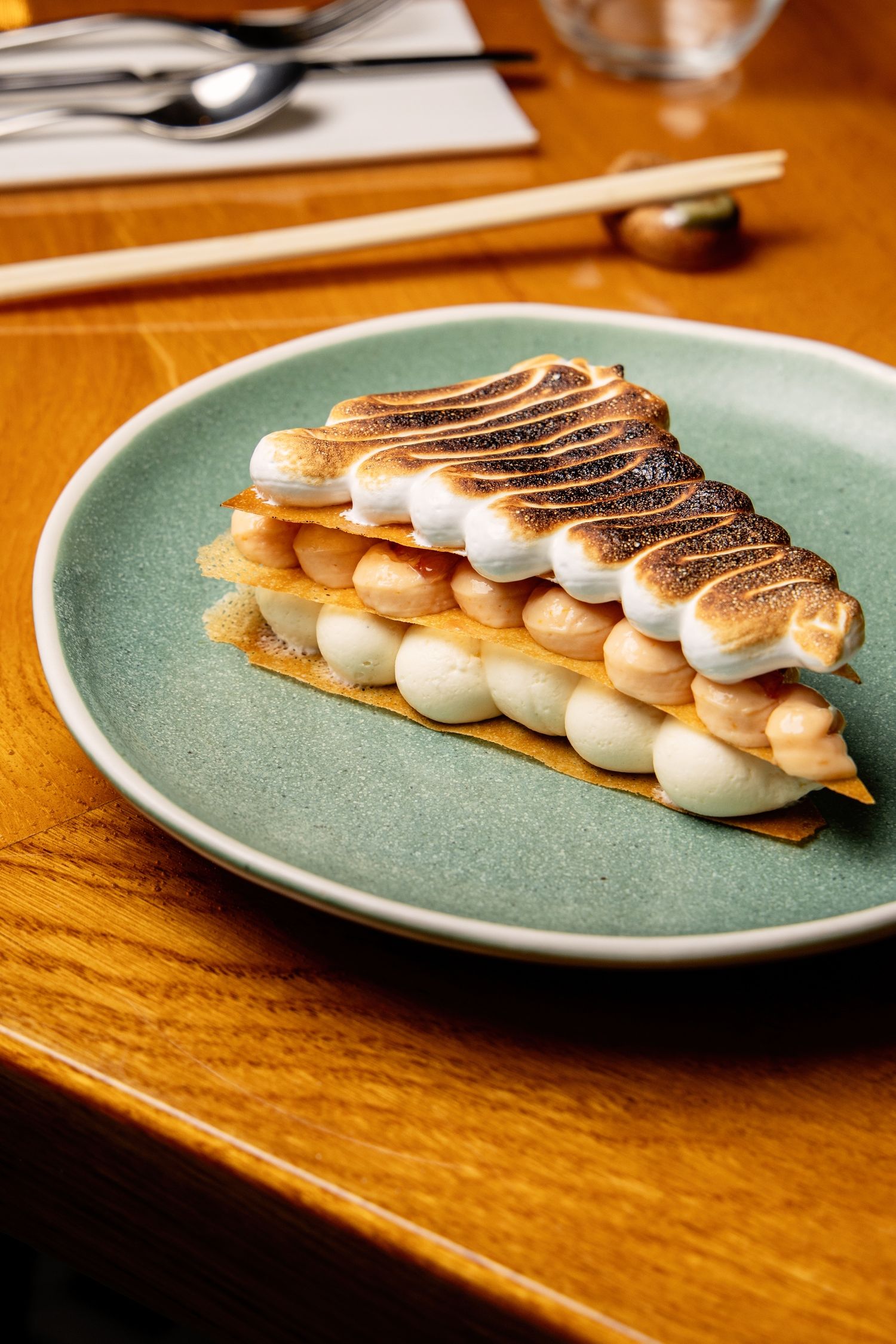 A slice of meringue tart with toasted marshmallow topping served on a turquoise plate on a wooden table.