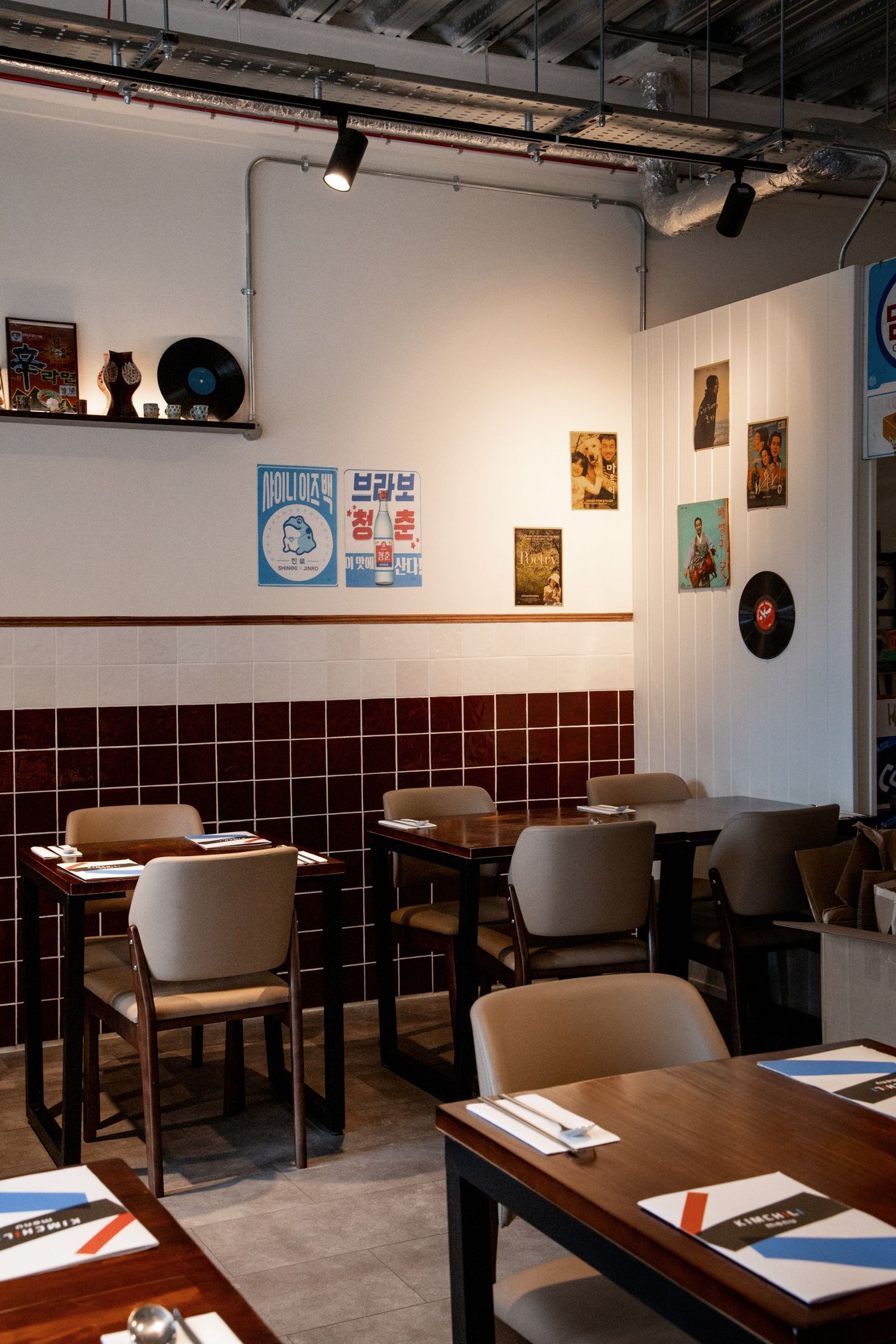 Cozy Korean restaurant interior with dark red tile walls, vinyl records decor, wooden tables, and vintage posters.