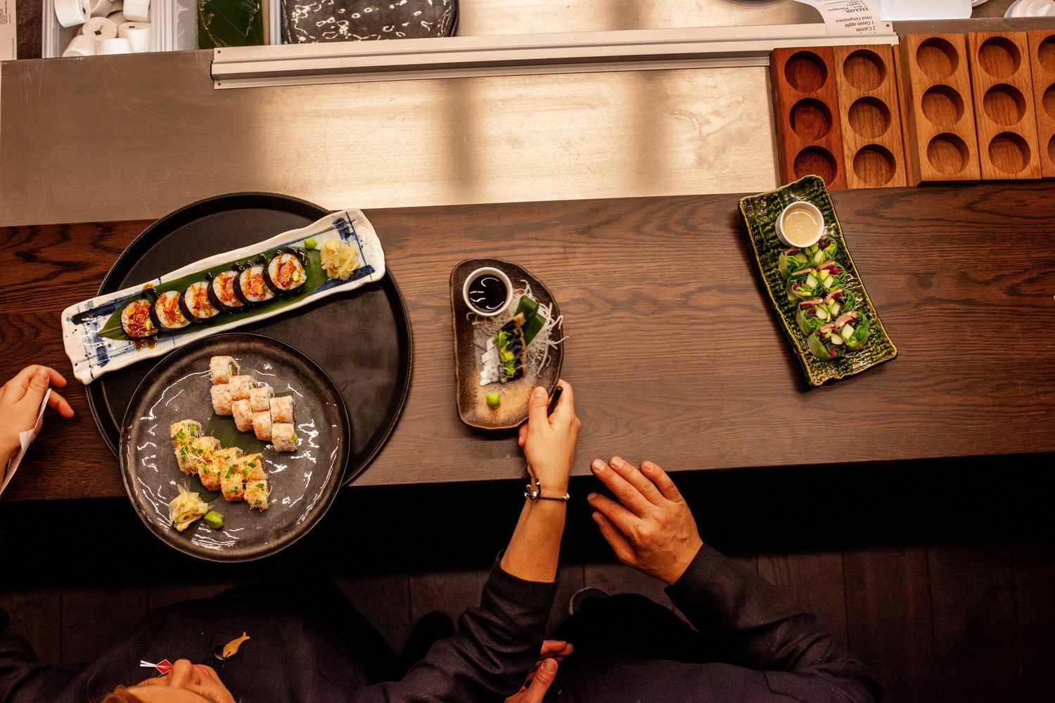 Overhead view of sushi rolls and appetizers on a dark wooden table at a Japanese restaurant.