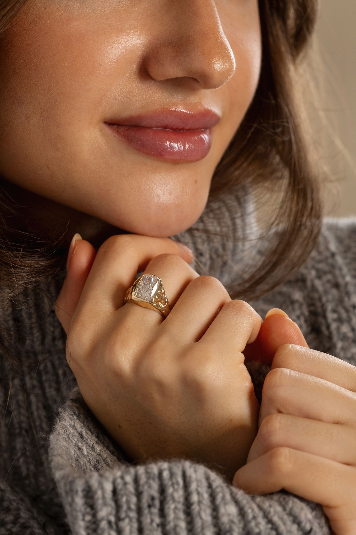 Close-up of a diamond engagement ring worn on a hand with a cozy gray knit sweater in the background.