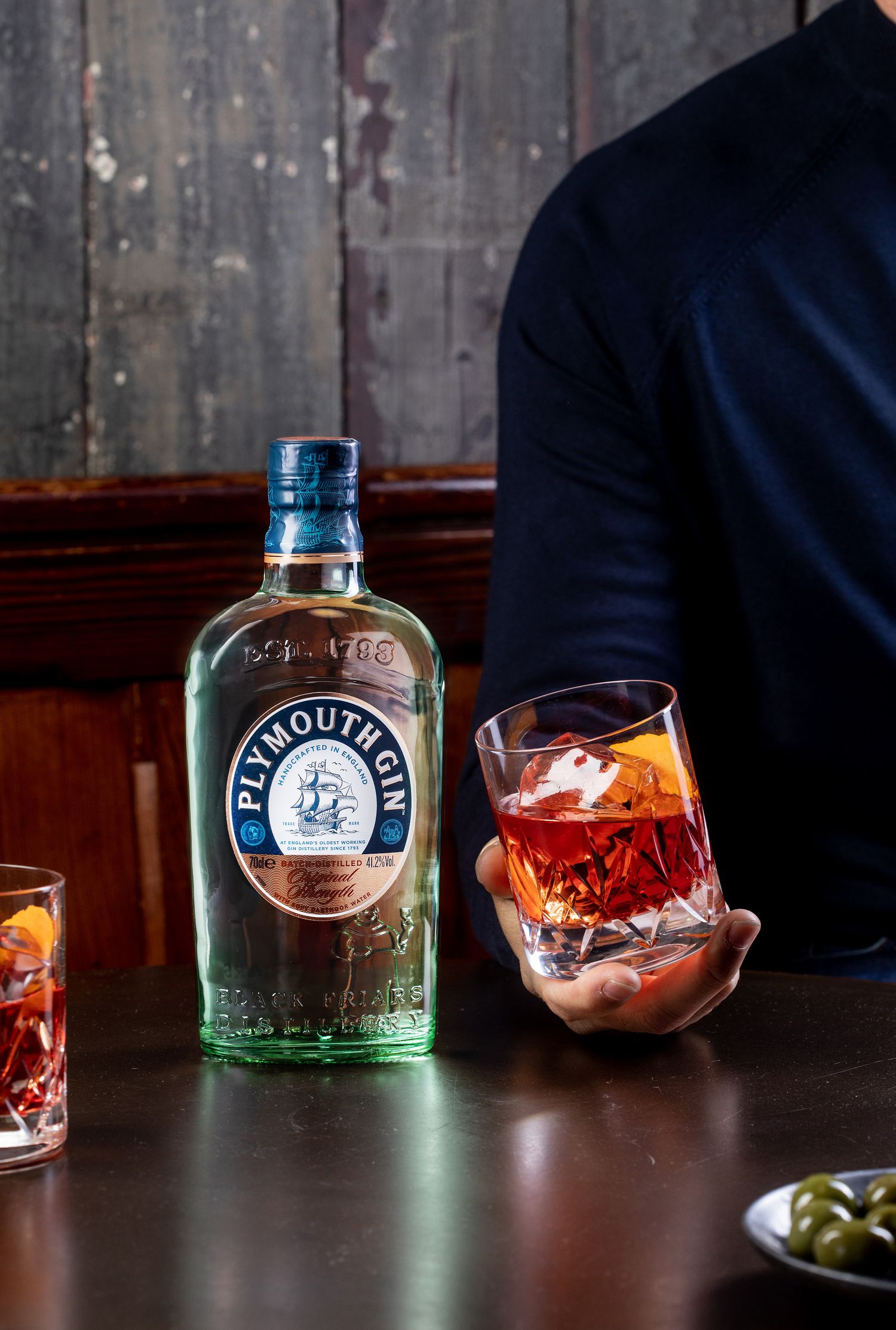 Plymouth gin bottle and cocktail glasses arranged on a dark wooden surface.